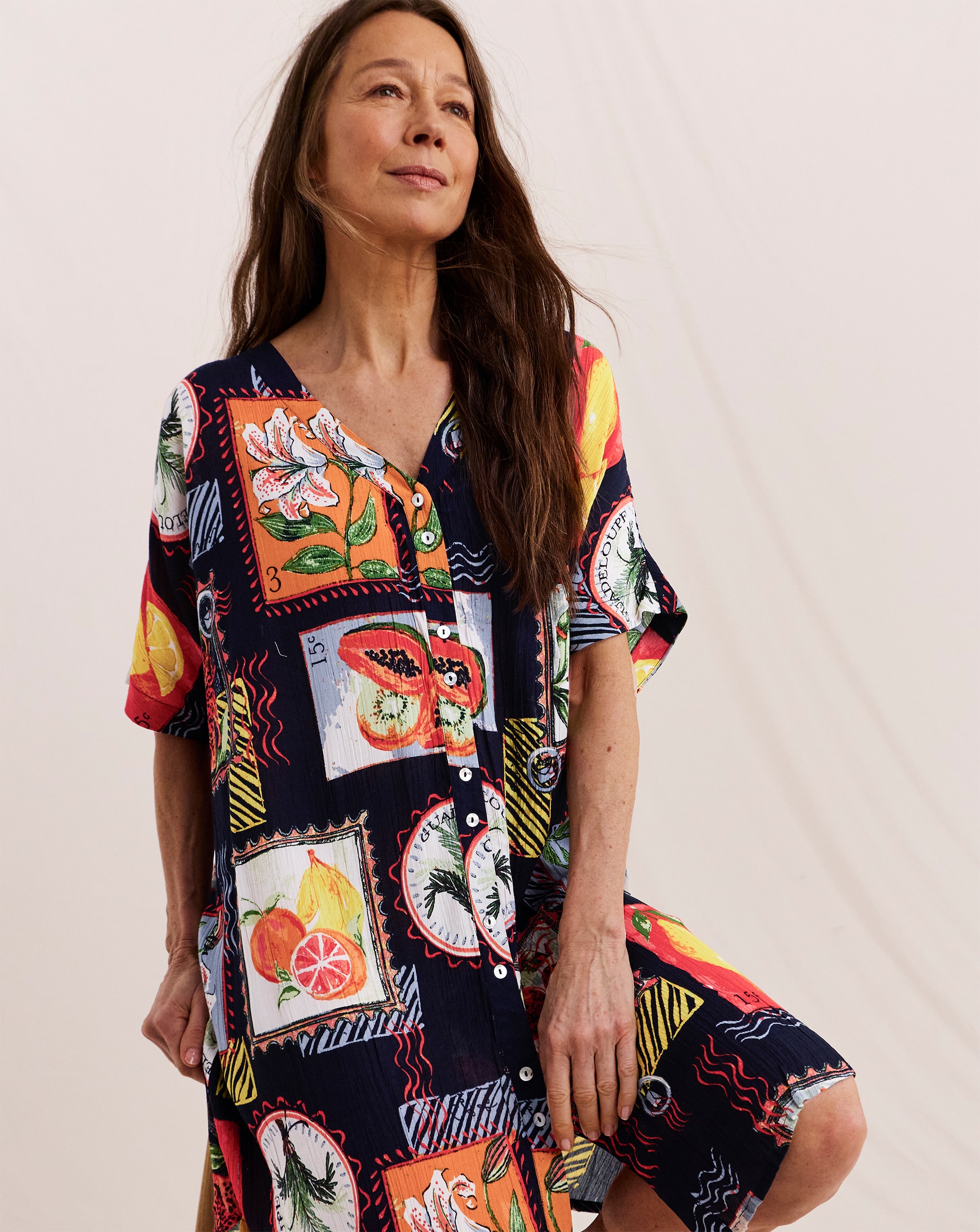 Person wearing a colourful, patterned button-down dress with floral and fruit motifs.