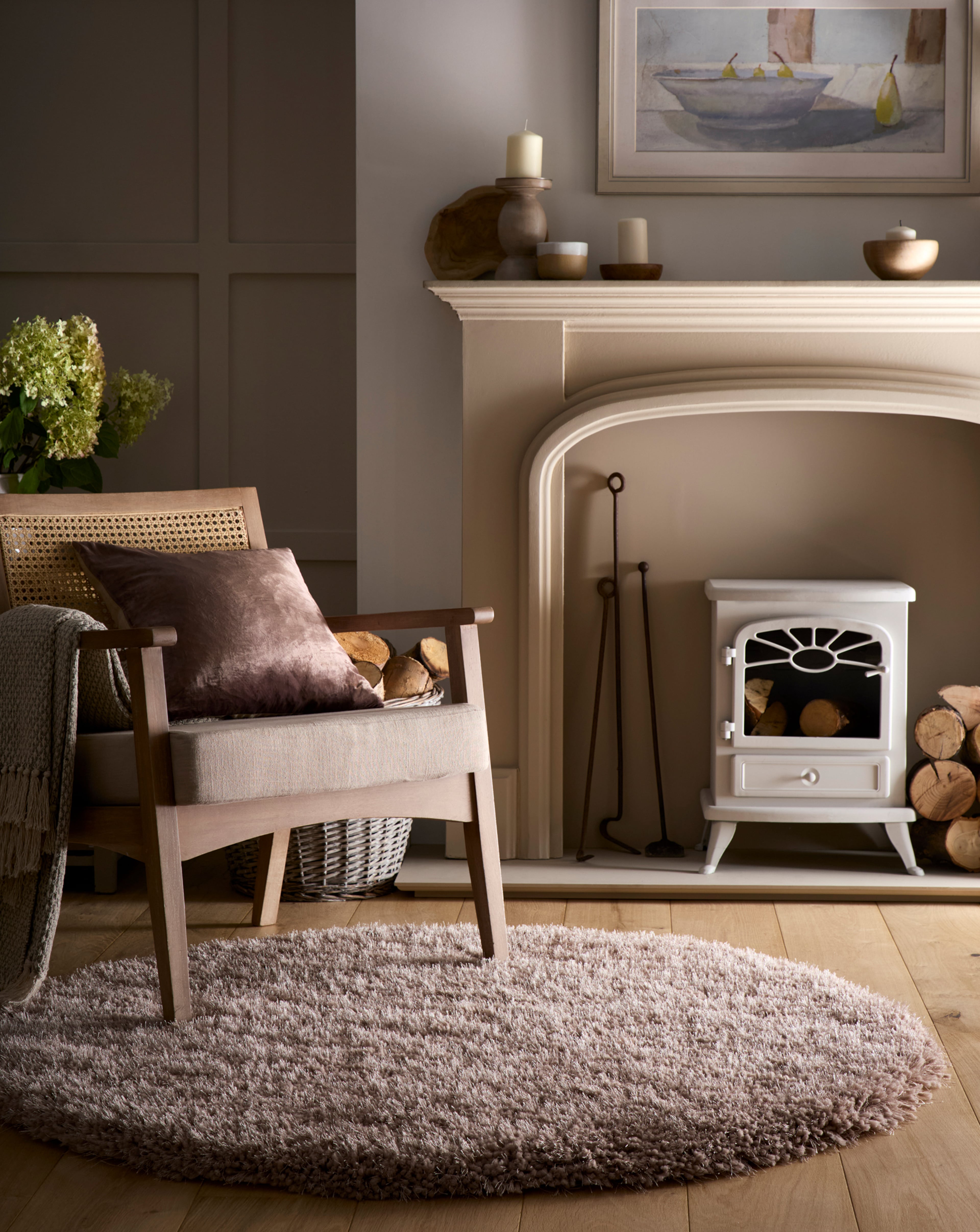 A neutral room set with a chair with cushion, a shaggy circle rug and fire place.