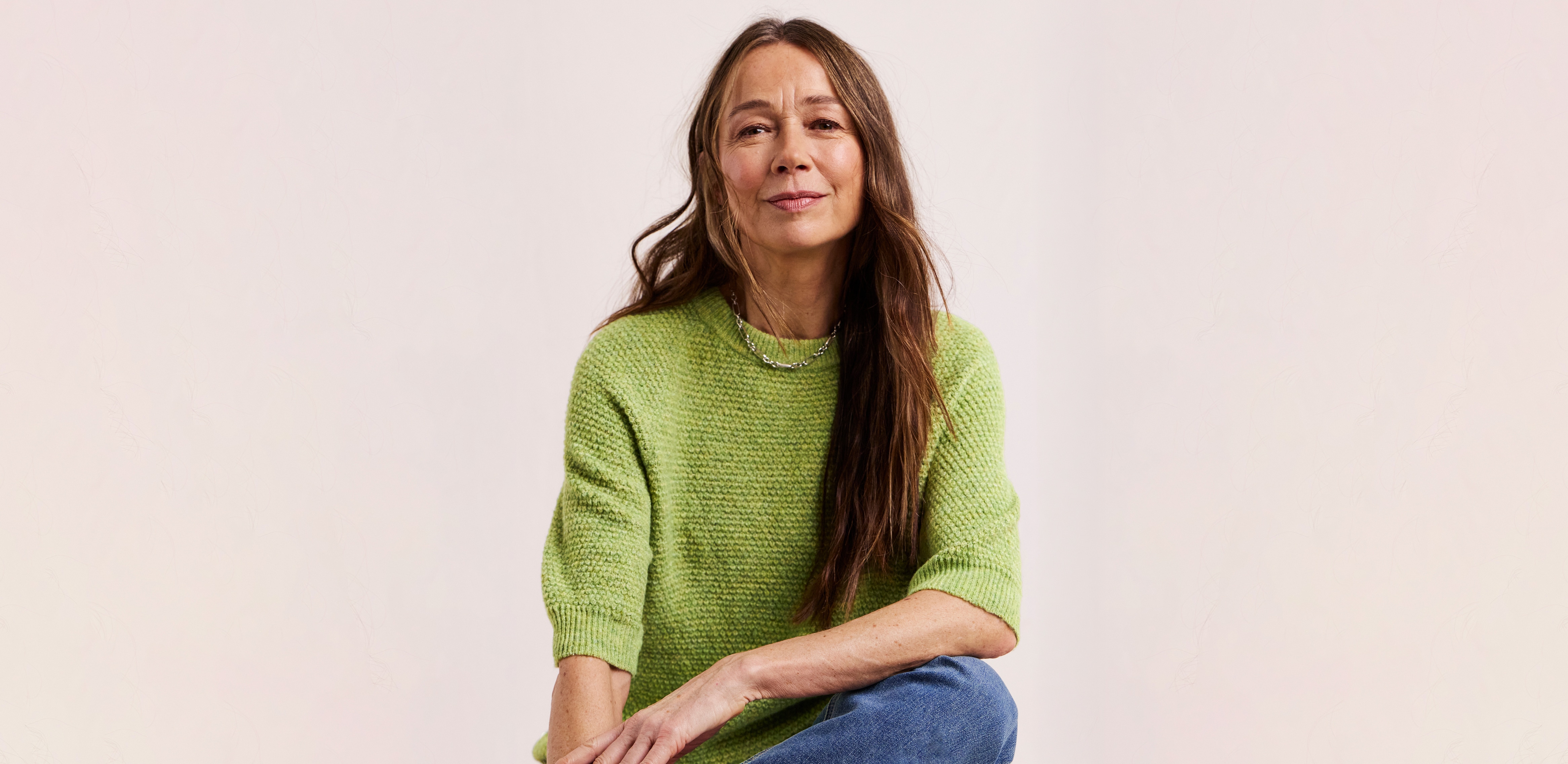 A model sat wearing a green Julipa short sleeve jumper and blue jeans