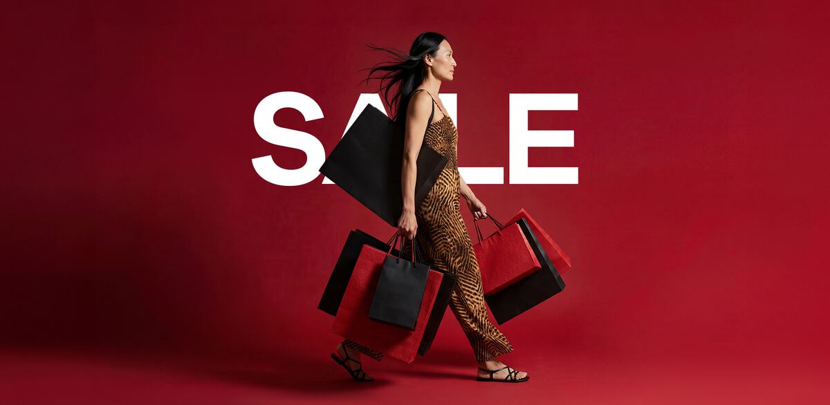 Person walking across a red background carrying multiple red and black shopping bags.