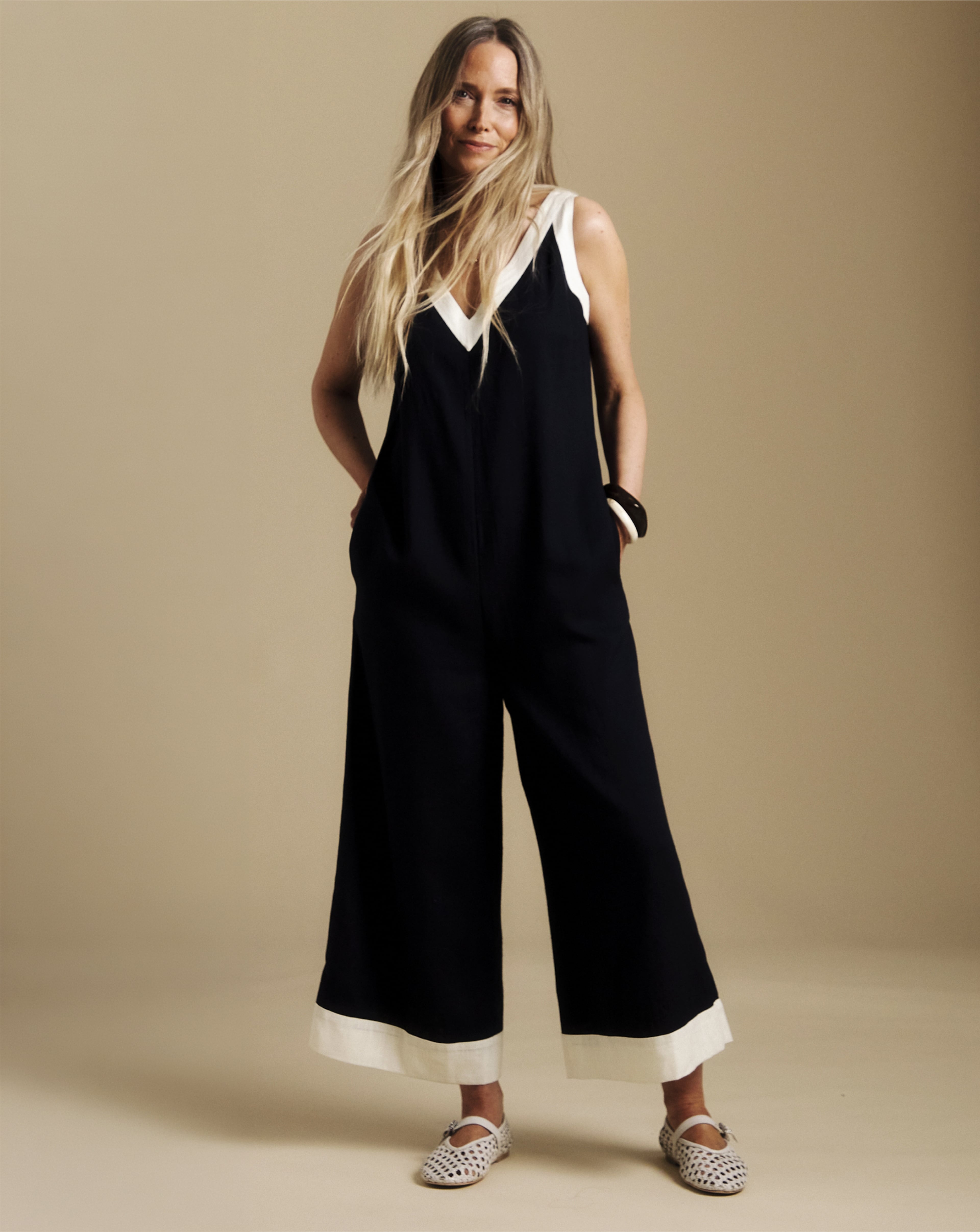 Person wearing a sleeveless black jumpsuit with white trim and wide legs, paired with light woven flat shoes.