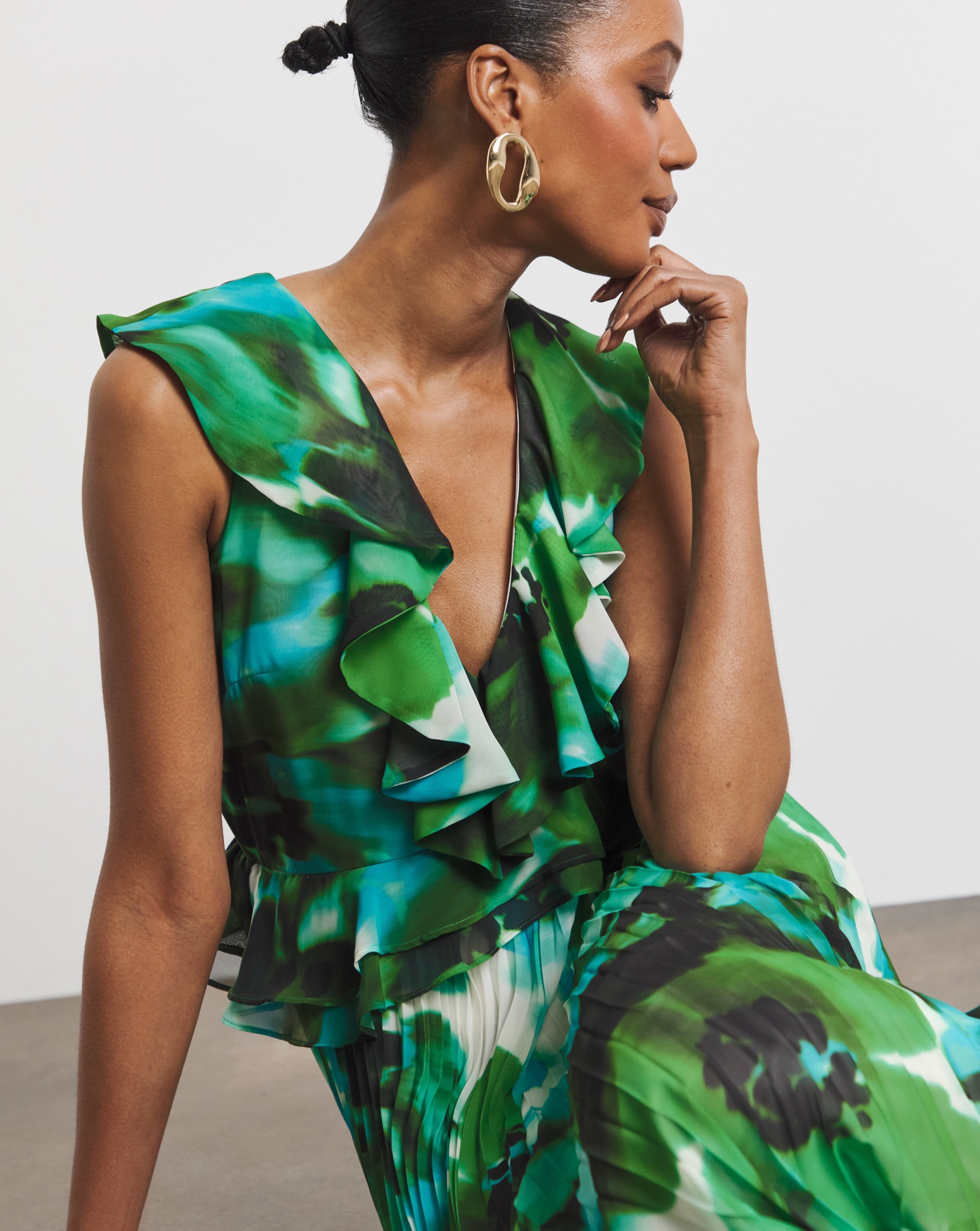 Person in a flowing green patterned dress with ruffled neckline, wearing oversized gold hoop earrings.