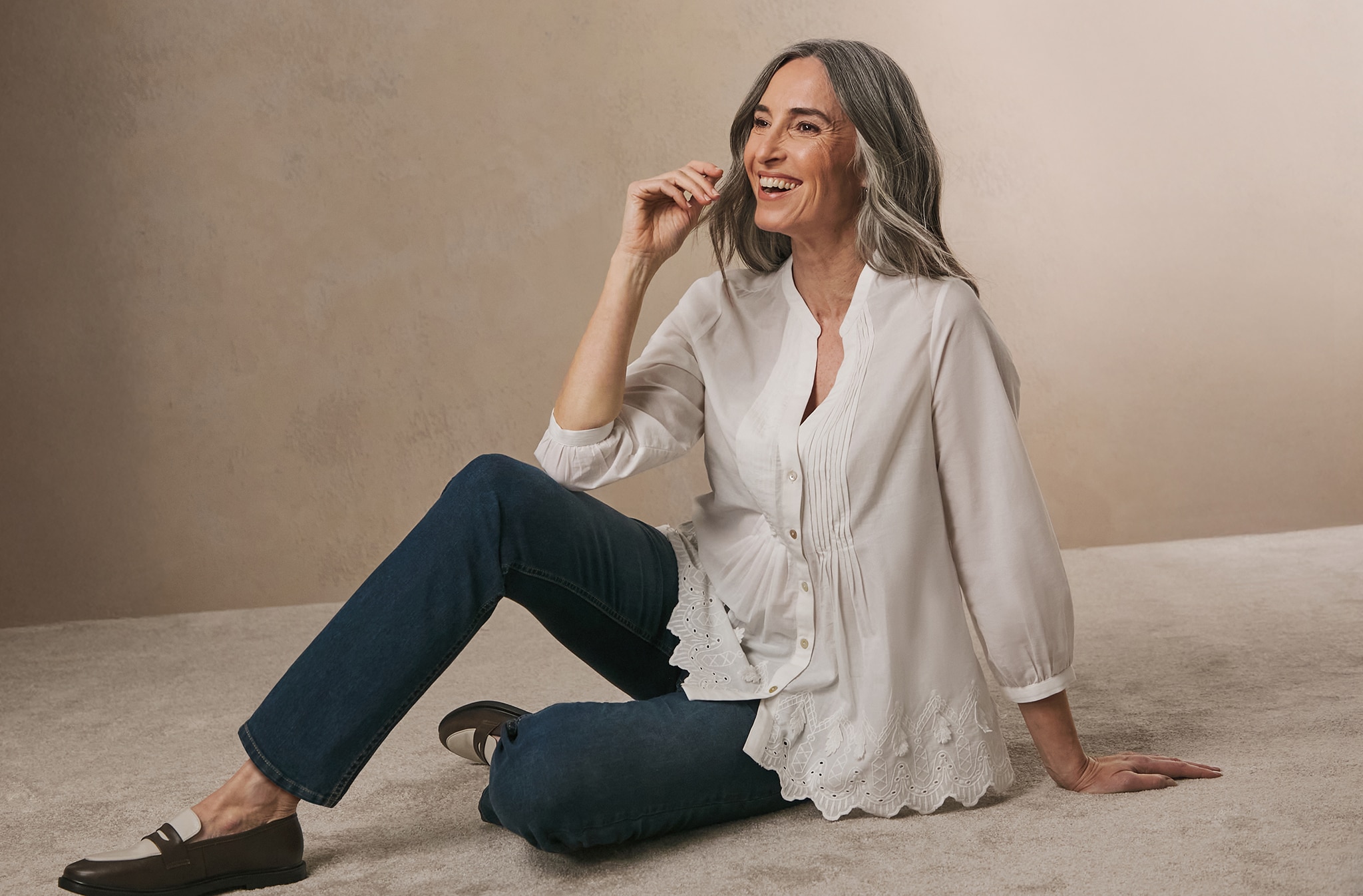 A woman sat on the floor wearing jeans and a taupe loose fitting blouse