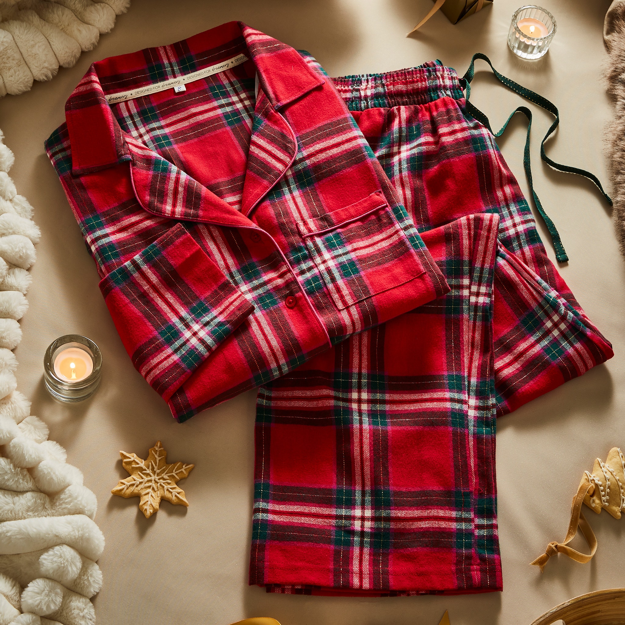 Red plaid pyjama set laid out on a table with candles and snowflake decorations.