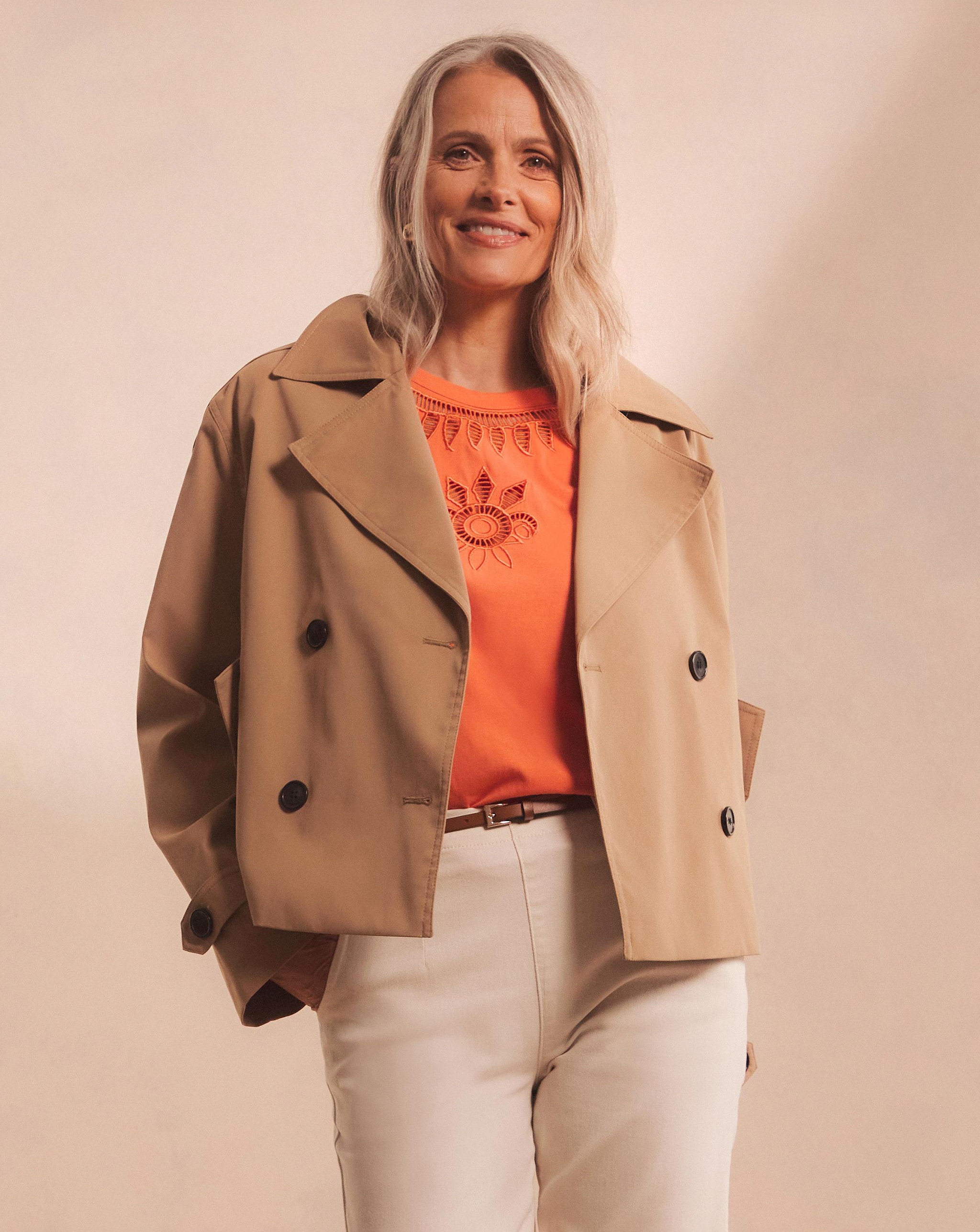 Model wearing a brown jacket over an orange t-shirt and white jeans