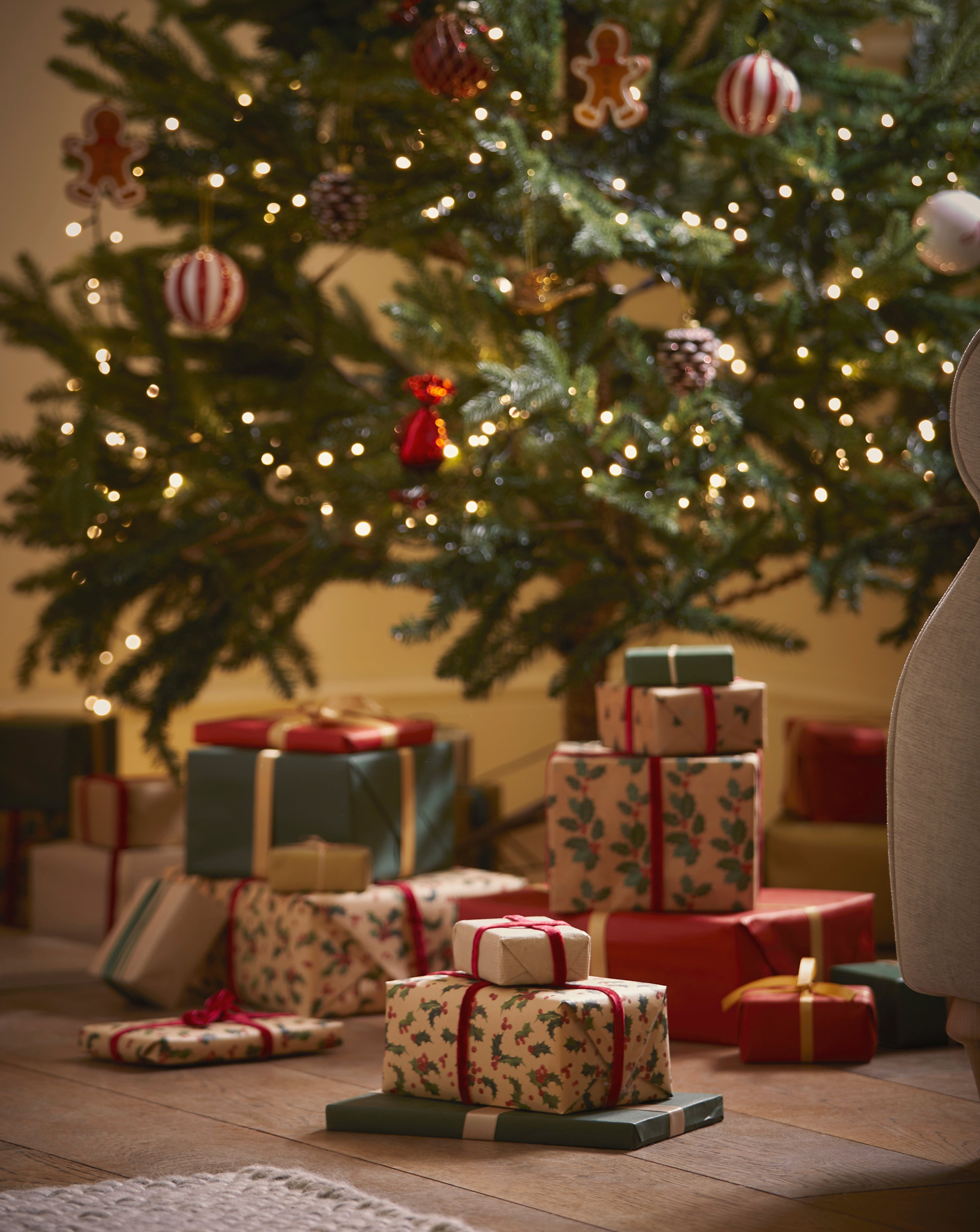 Wrapped presents on a wooden floor in front of a decorated Christmas tree with lights and ornaments