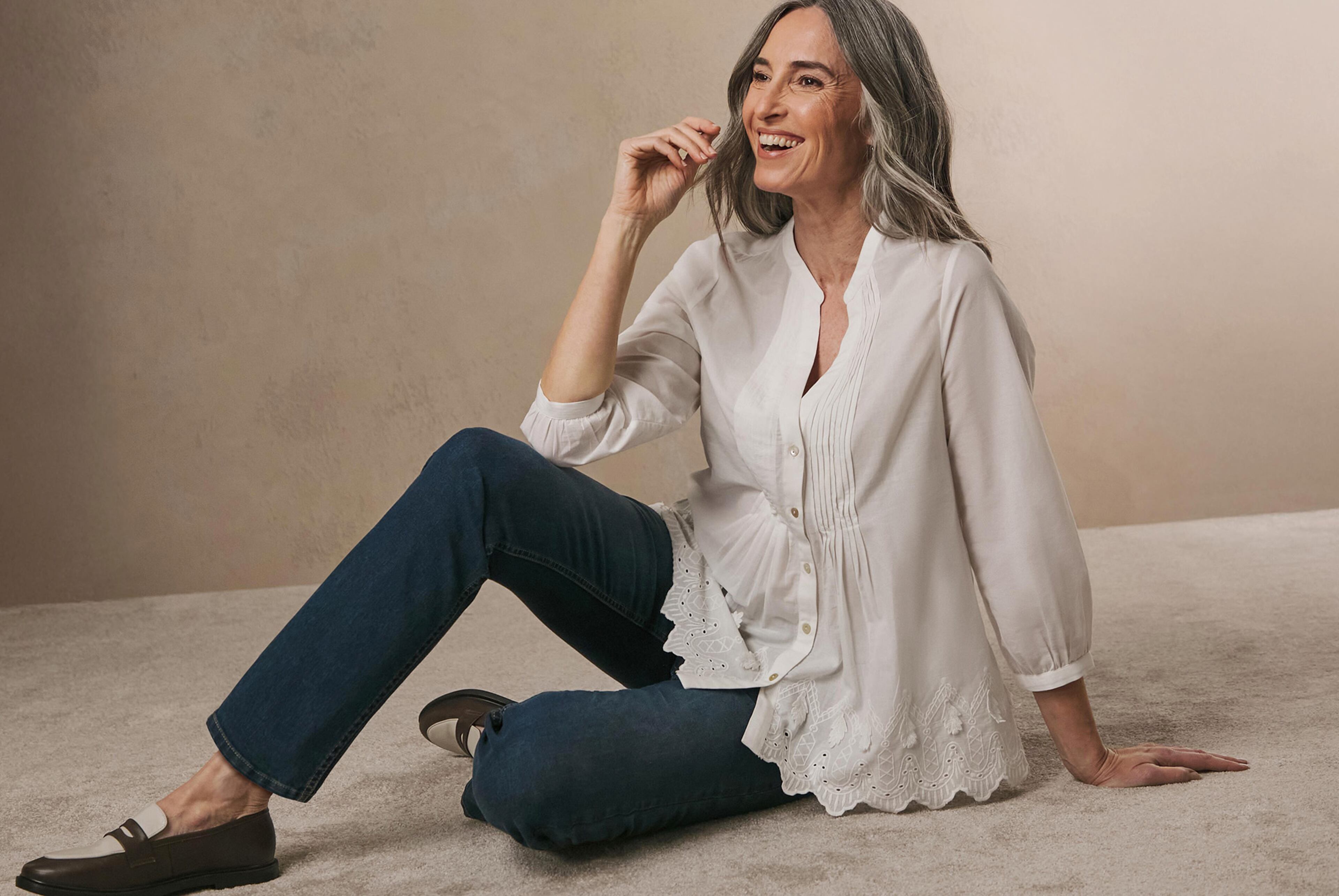 A woman sat on the floor wearing a white blouse and jeans