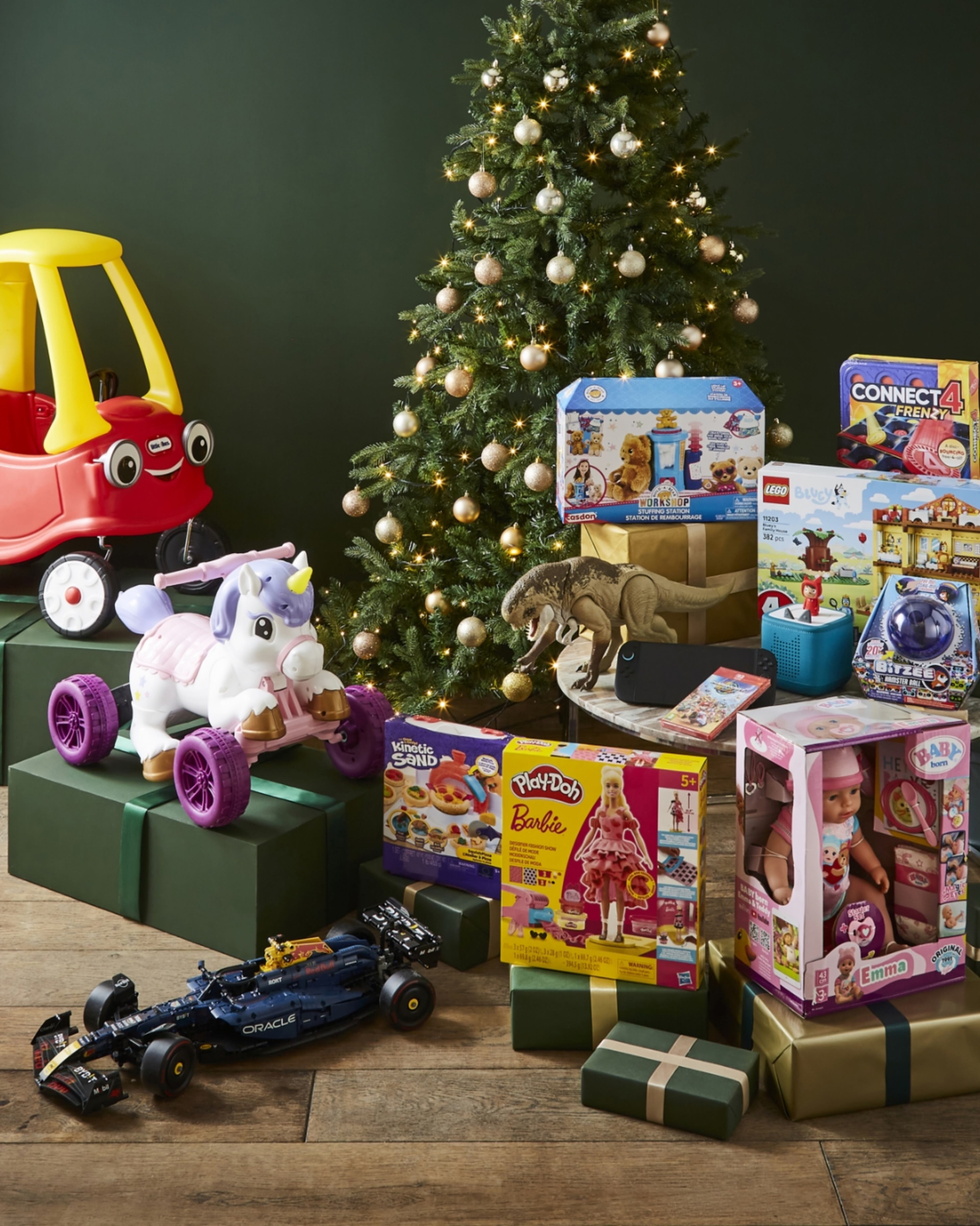 Christmas toys and gifts for kids: Little Tikes Cozy Coupe, unicorn ride-on, Barbie doll, and board games under a decorated tree.