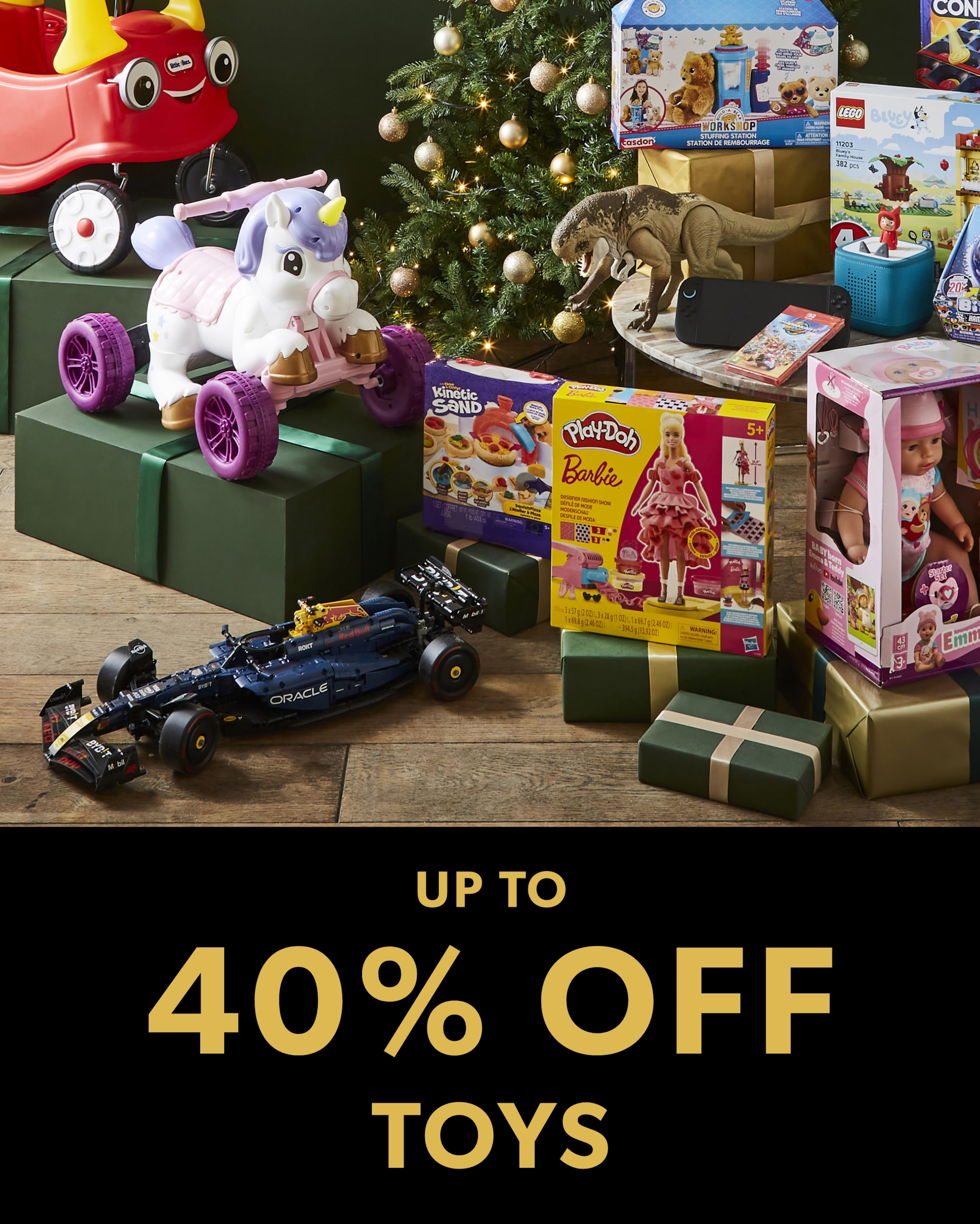 A festive display of popular toys, including a race car, unicorn ride-on, Barbie, Kinetic Sand, and a dinosaur, arranged around a Christmas tree with the text "UP TO 40% OFF TOYS"