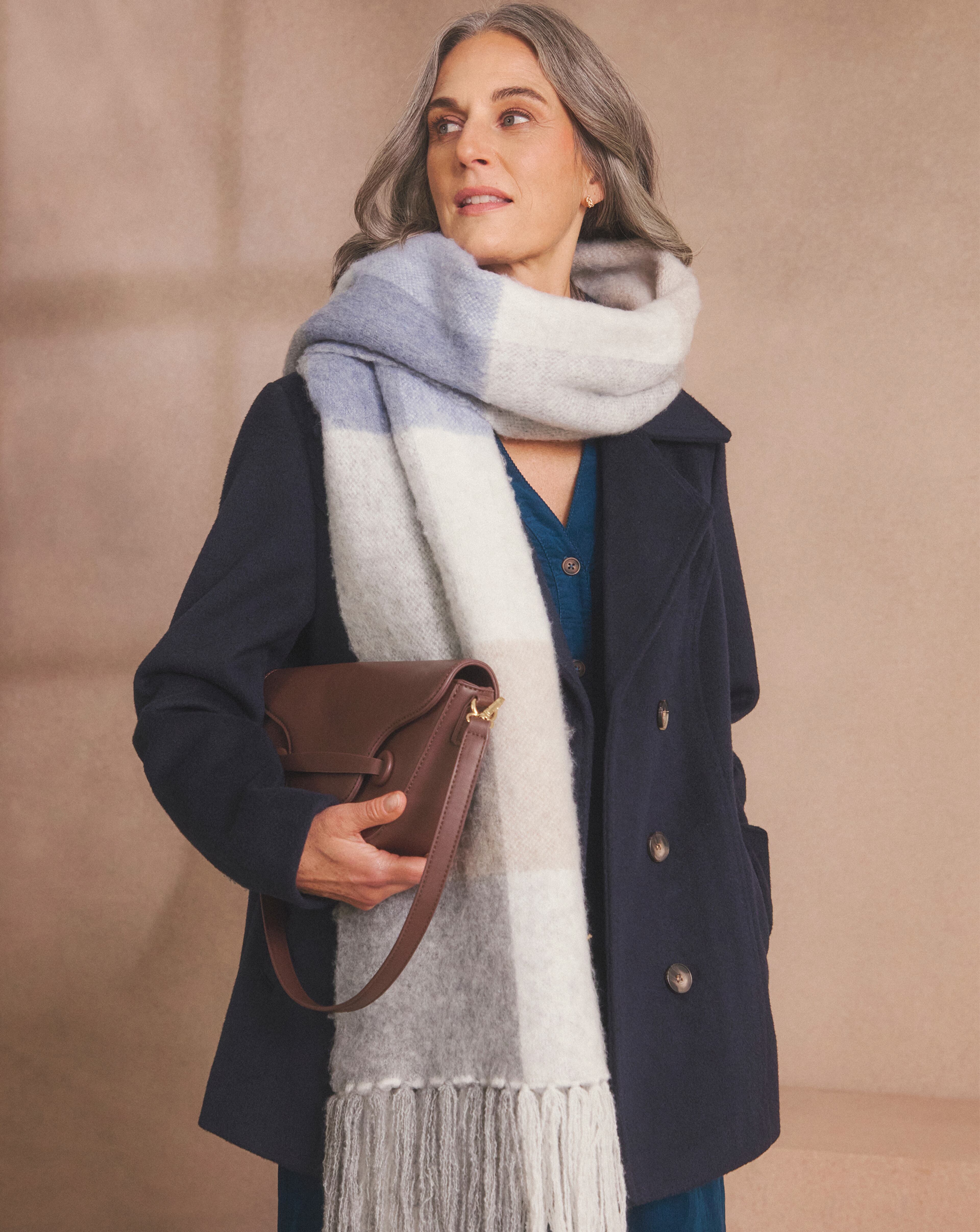 Person in a dark blue coat with a striped scarf, holding a brown leather handbag.