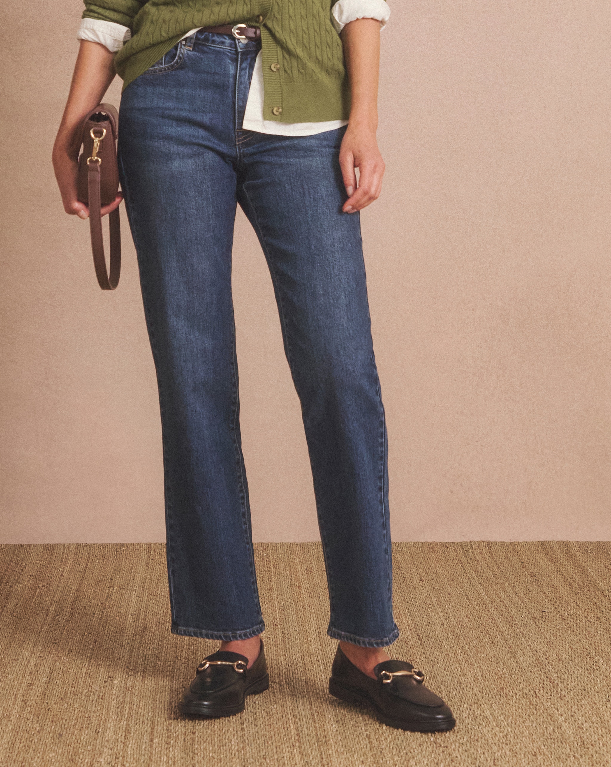 Person in jeans, a white shirt, and green cardigan holding a small brown handbag.