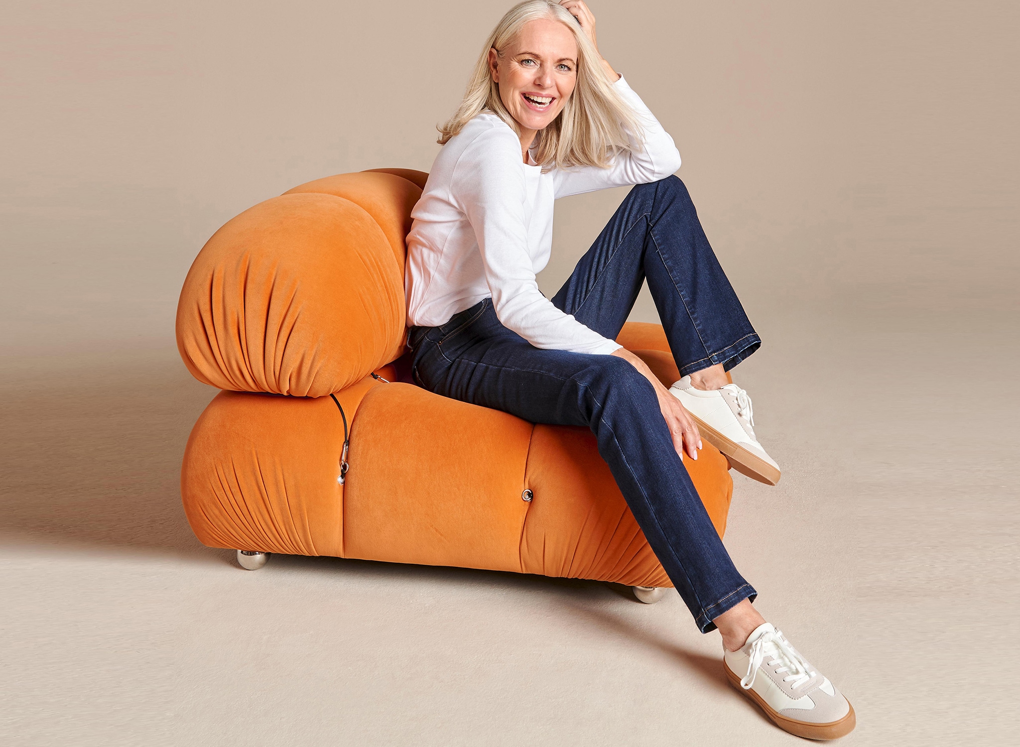 A woman sat on an orange modern chair in white top and jeans