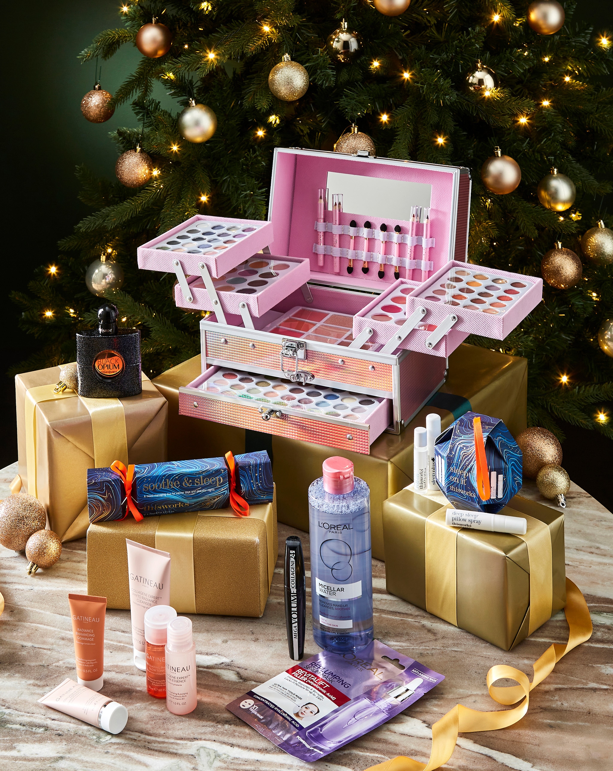 A selection of beauty products on a table, in front of a Christmas tree.
