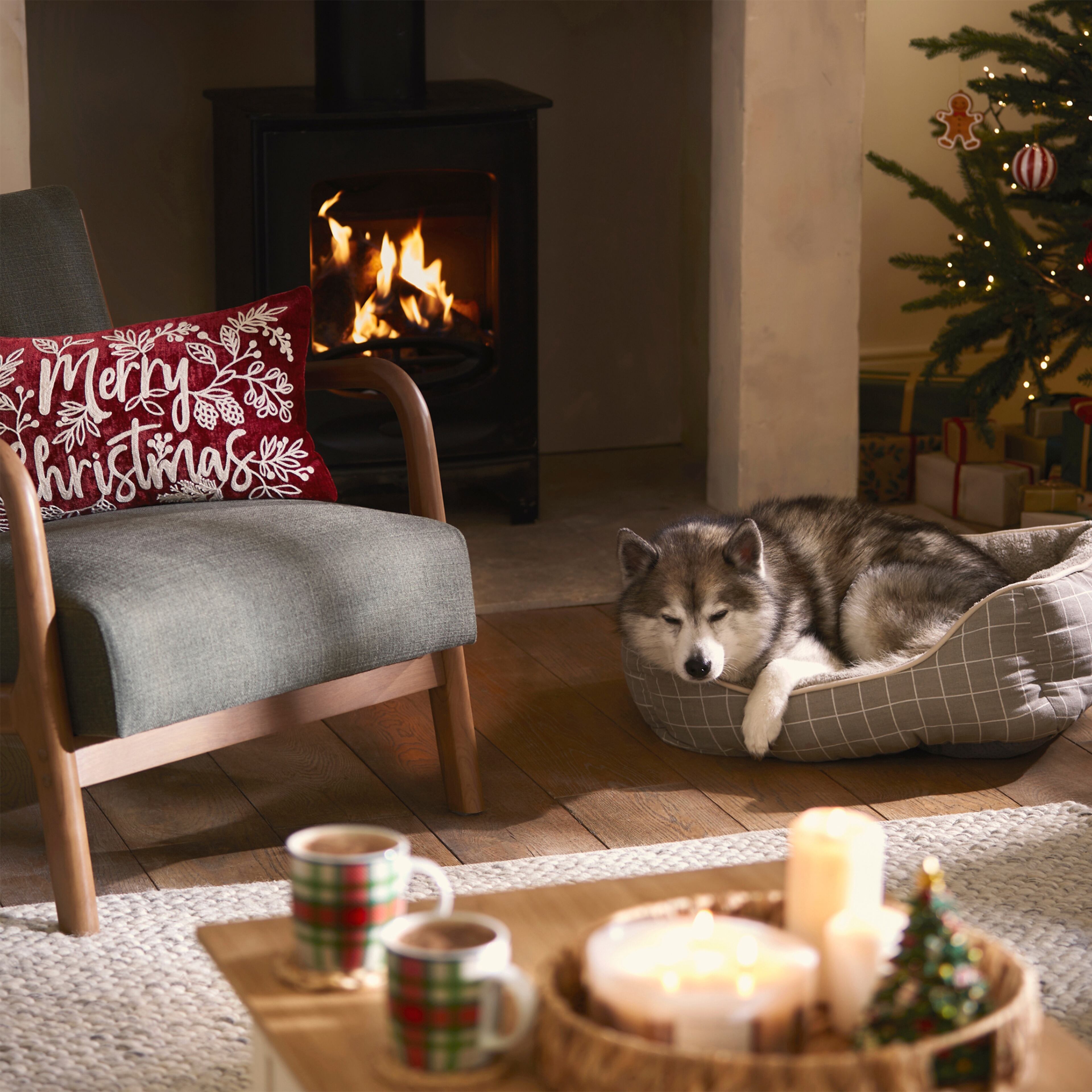 A grey armchair in front of the fire, with a red Christmas cushion.