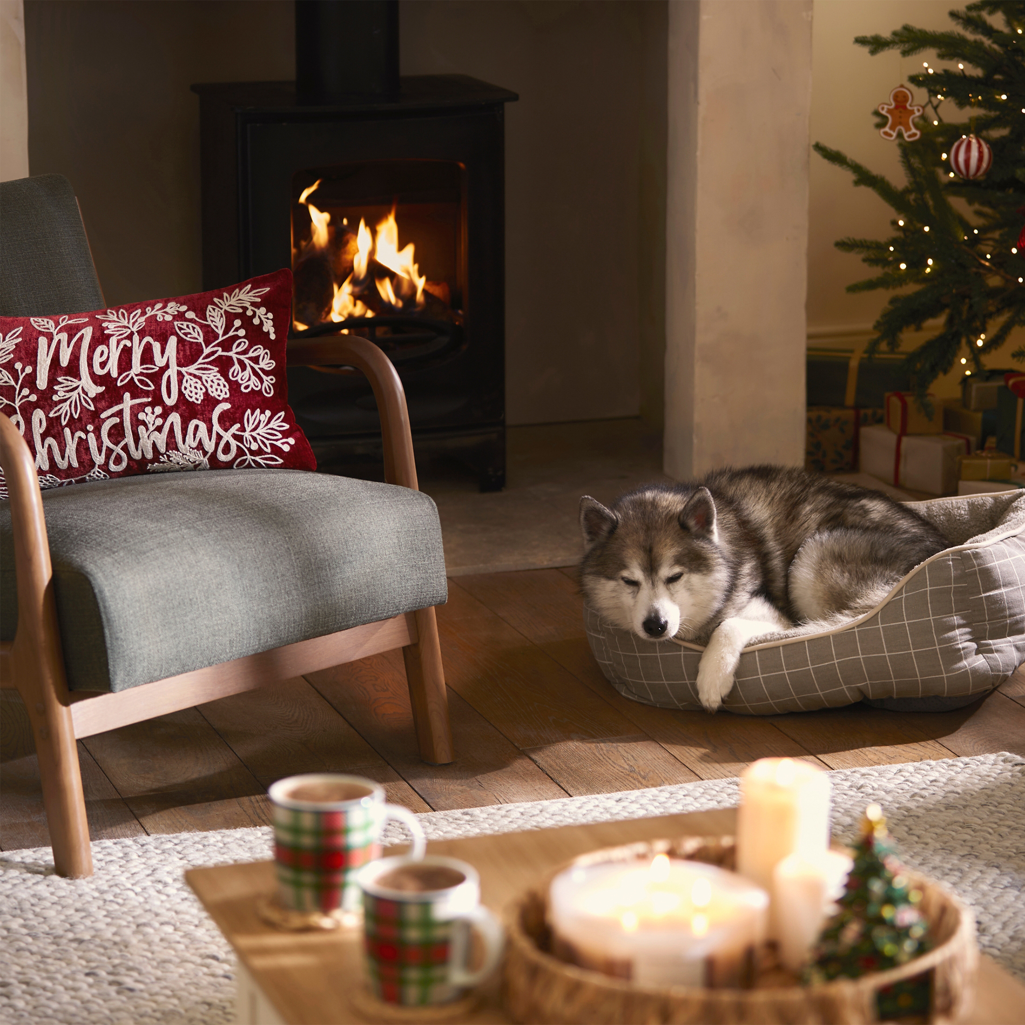 A grey armchair in front of the fire, with a red Christmas cushion.