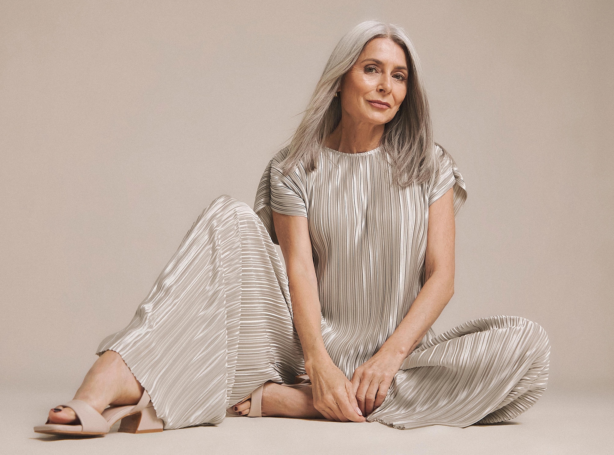 A woman sat on the floor wearing a shiny striped khaki trouser suit