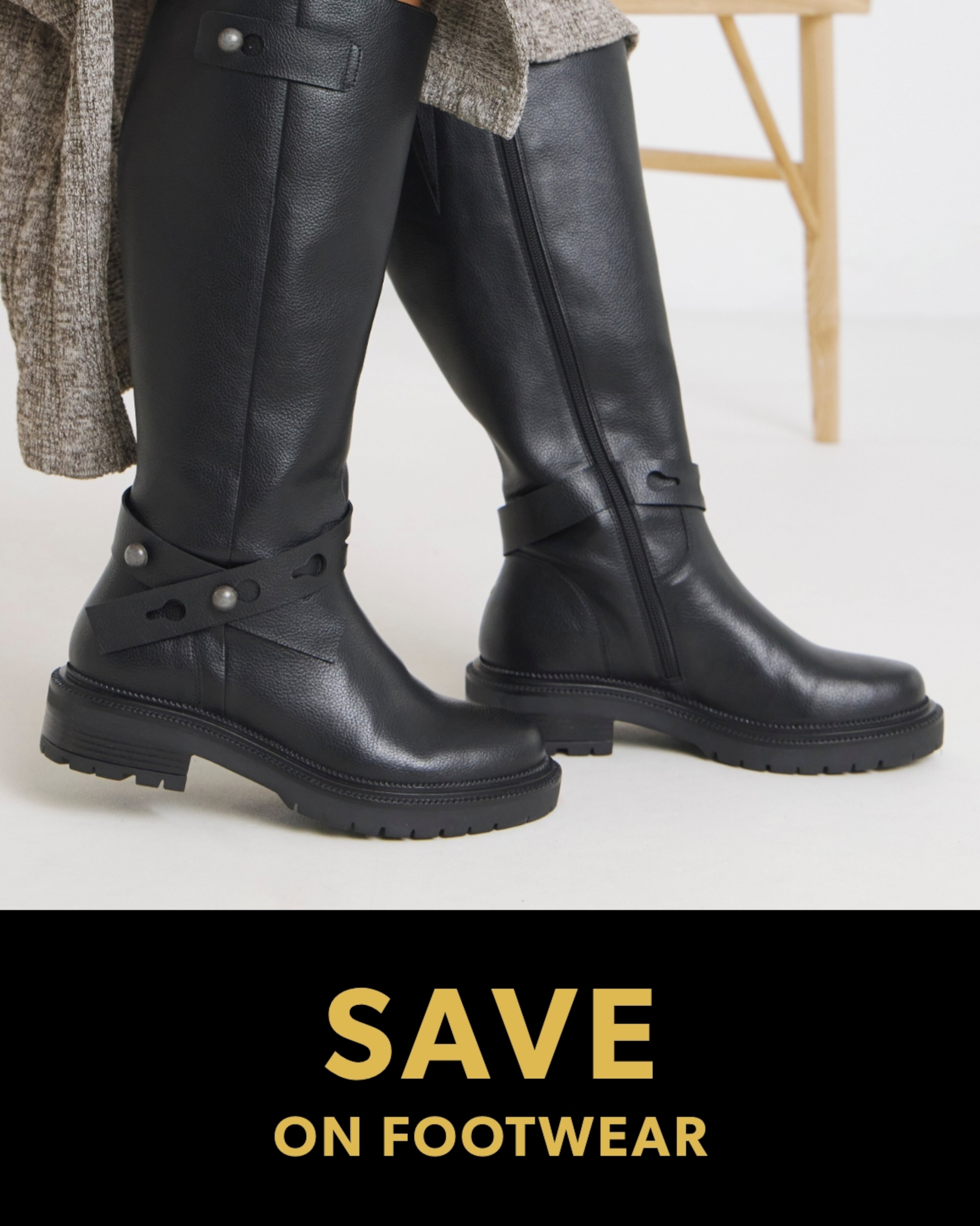 A close-up of a person wearing black leather knee-high boots with chunky soles and strap detailing, with the text "SAVE ON FOOTWEAR"