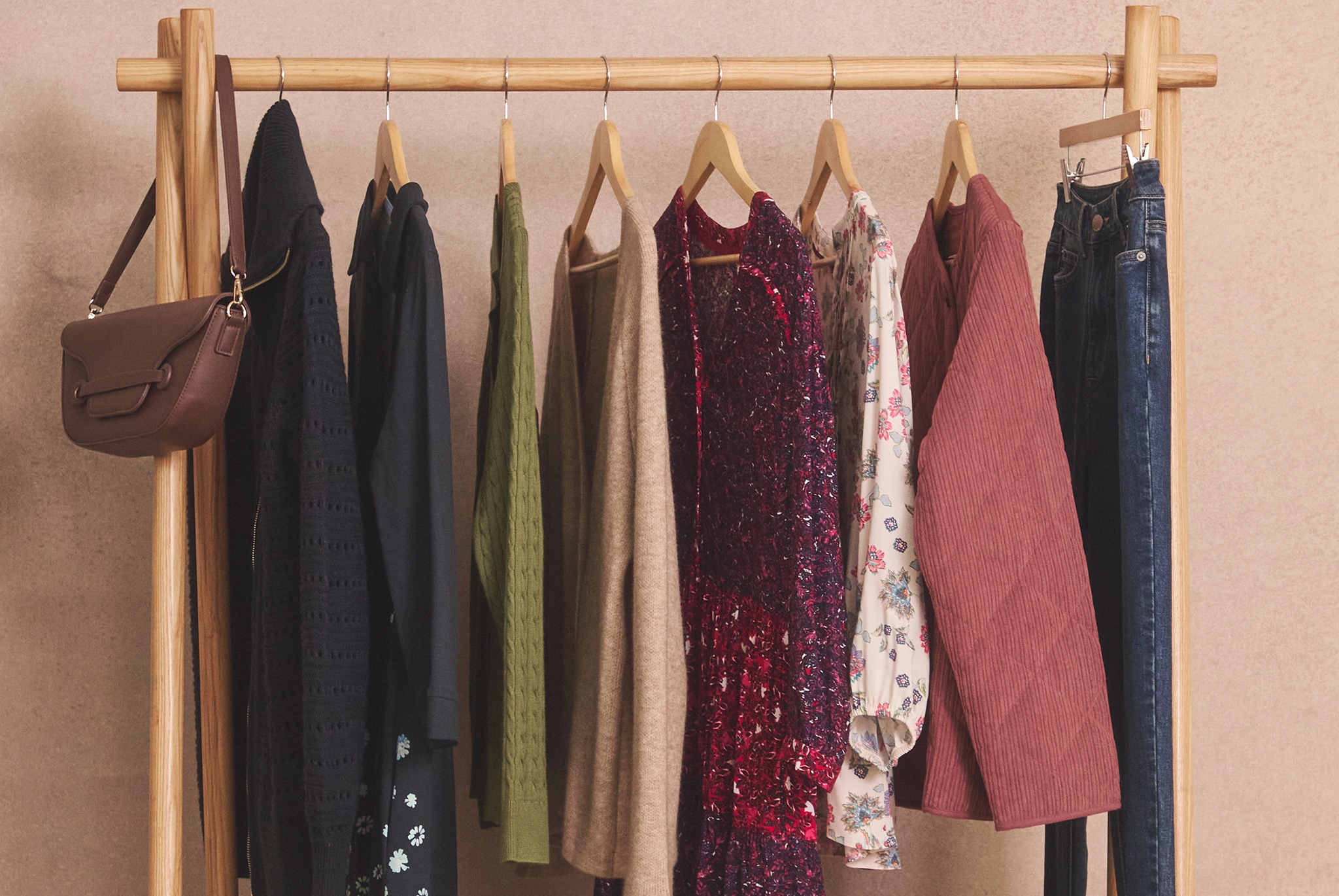 A wooden clothing rack displaying assorted garments and a brown handbag.