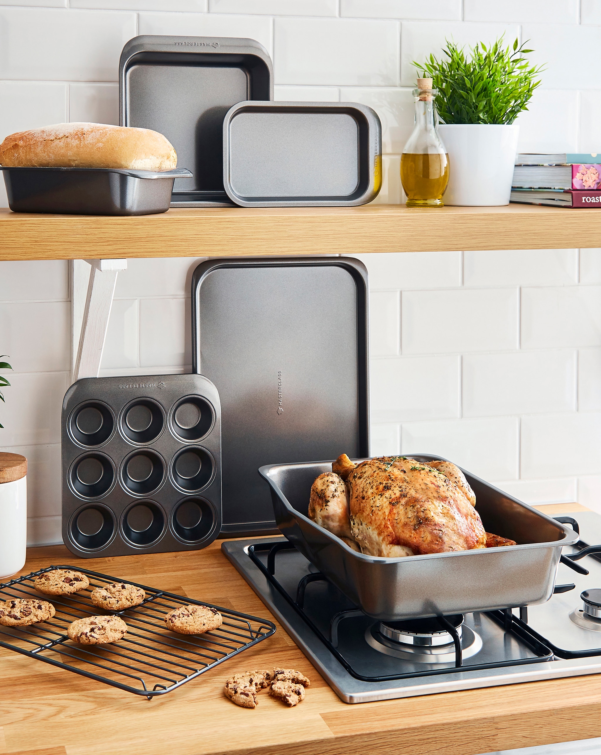 Kitchen scene with baking pans, roast chicken, chocolate chip cookies, and white subway tile background.