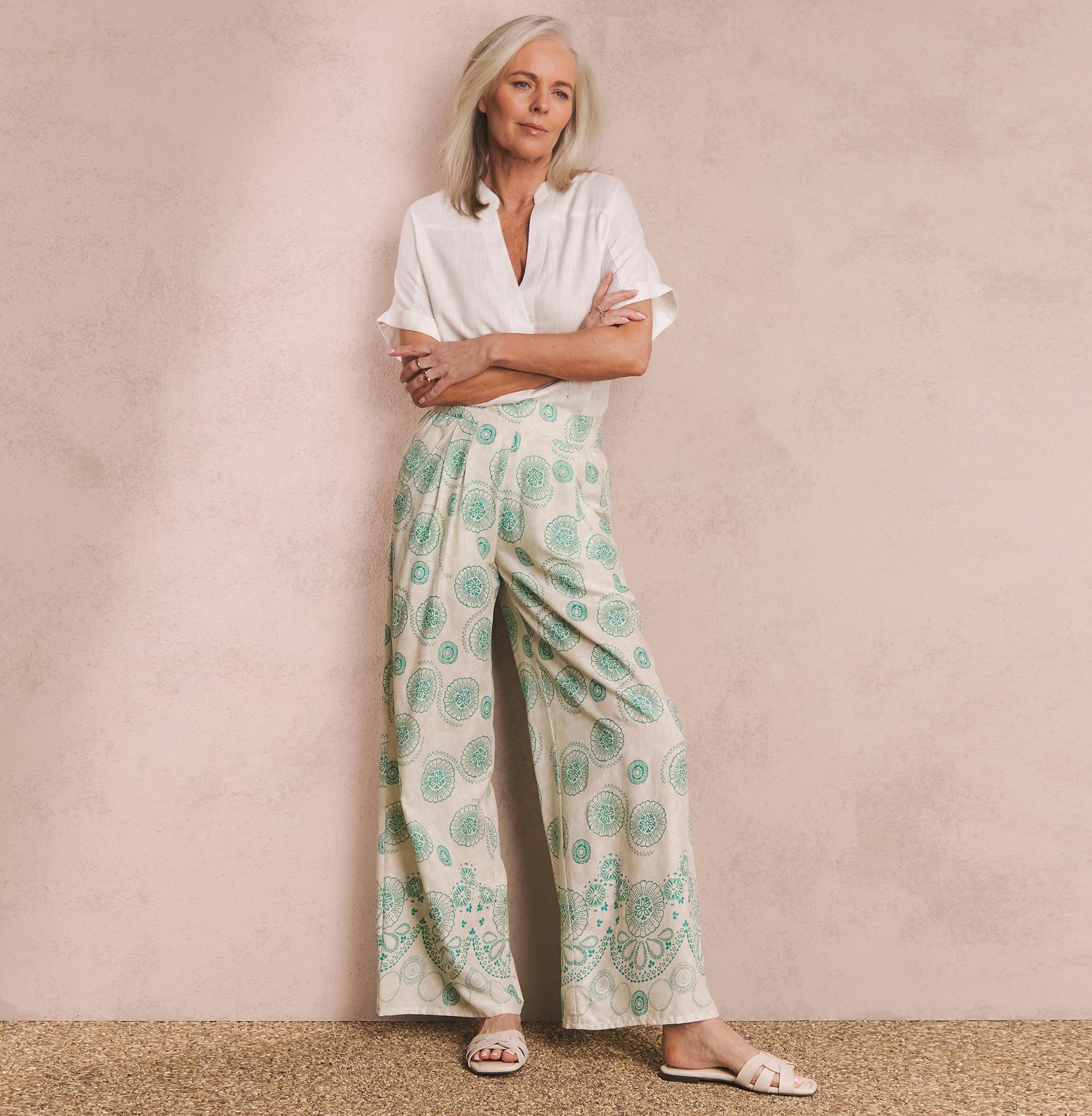 A woman stood wearing a short sleeved white blouse and green and white flared trousers