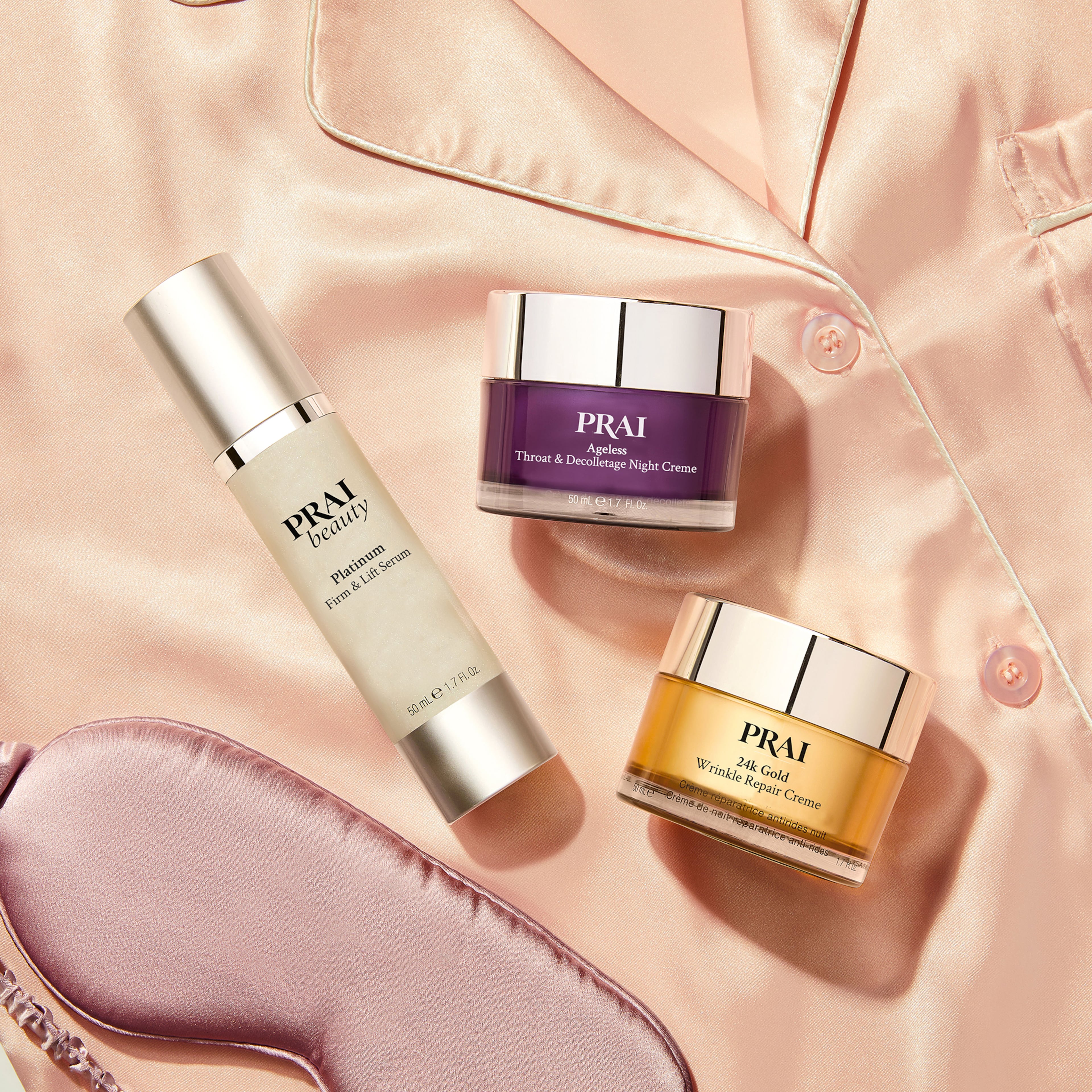 A selection of PRAI Beauty skincare products arranged on pink satin fabric