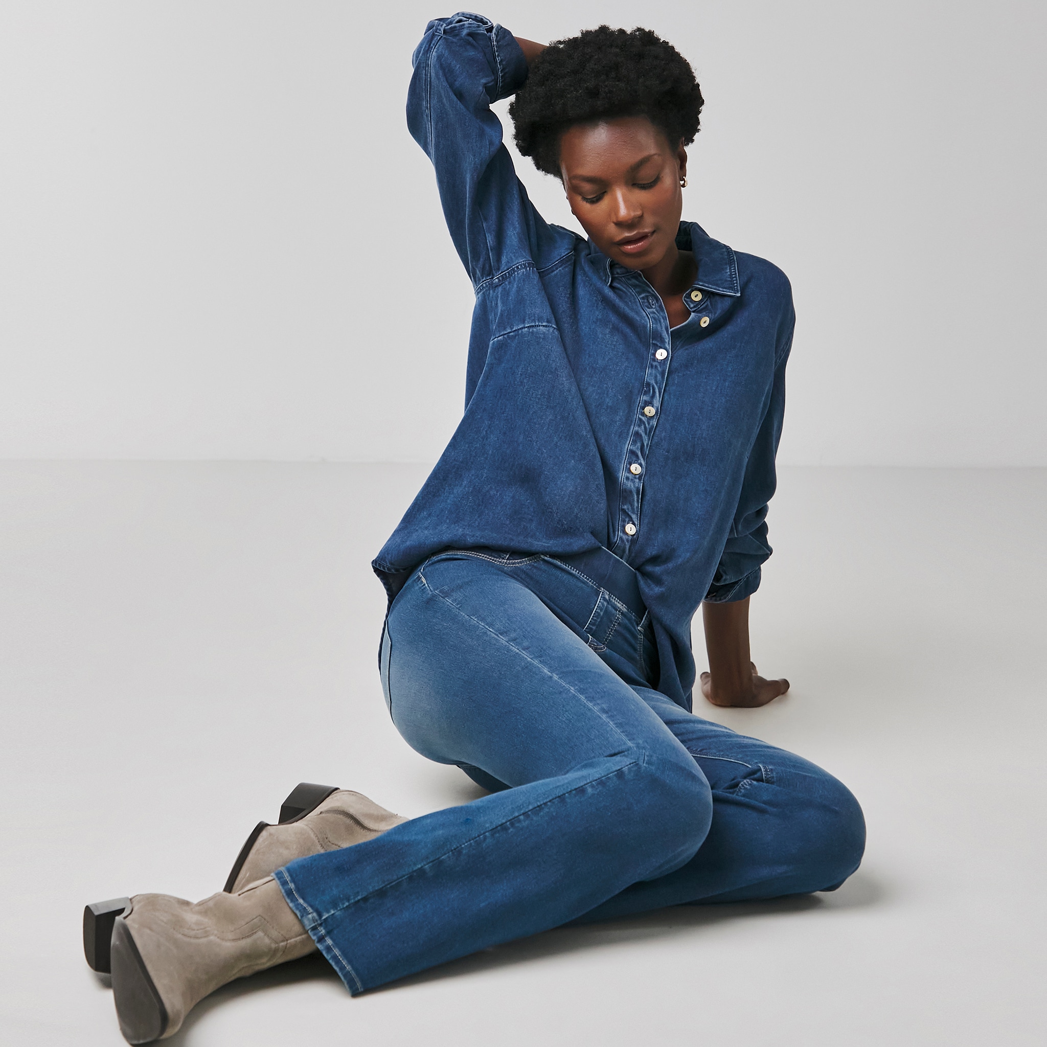 A woman sat on the floor wearing a denim shirt and jeans