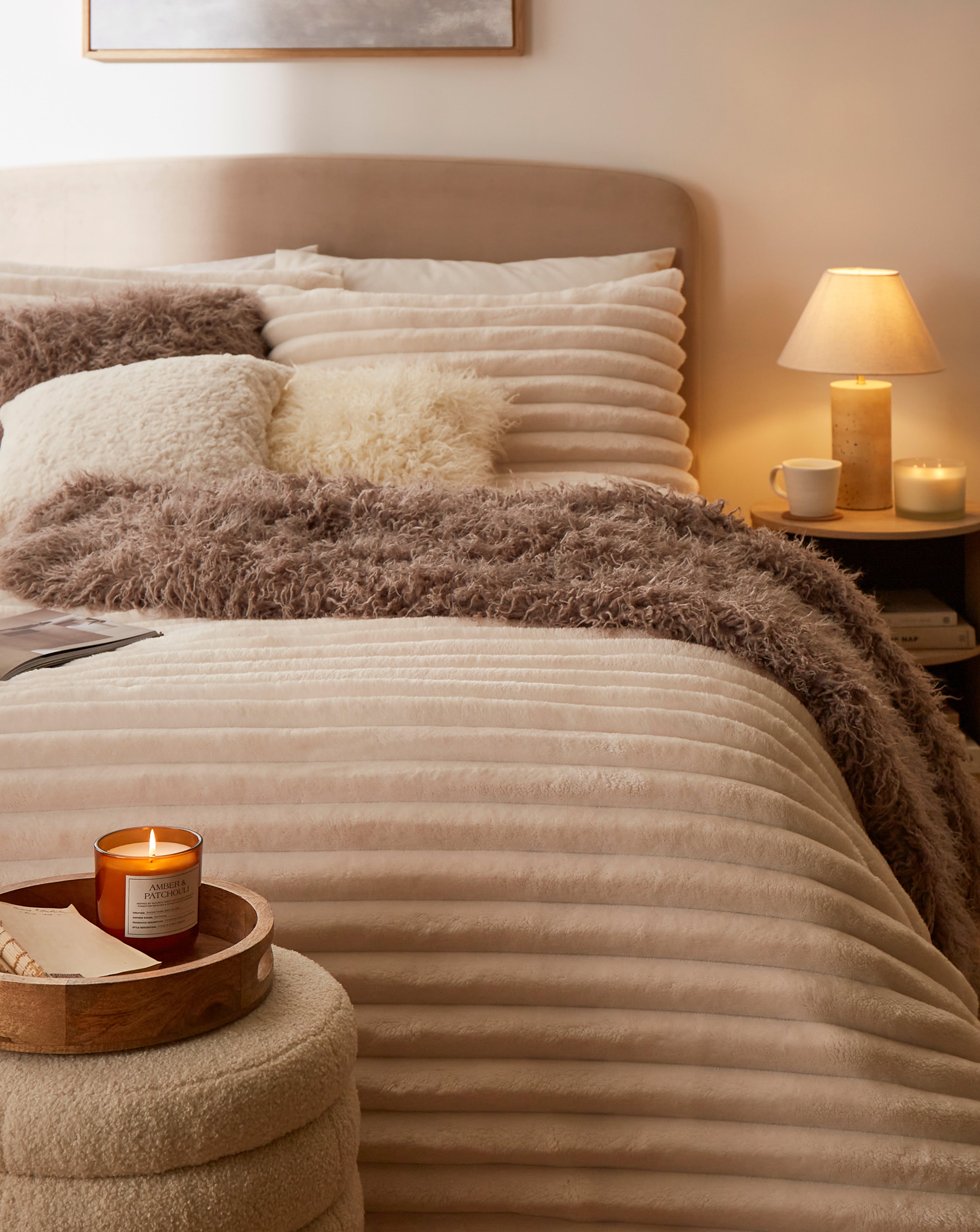 Cosy bedroom with a neatly made bed, soft lighting, and warm-toned decor including candles and a furry throw blanket