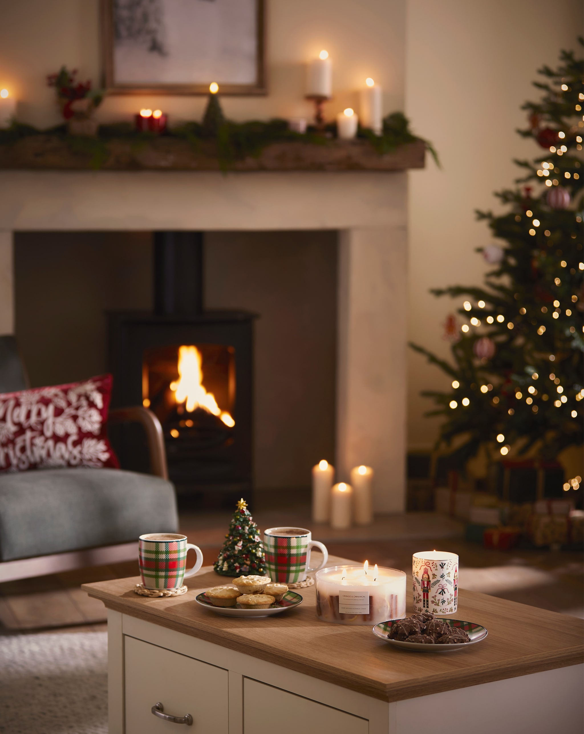 Living room with a lit fireplace, decorated tree, and coffee table with festive treats and candles.
