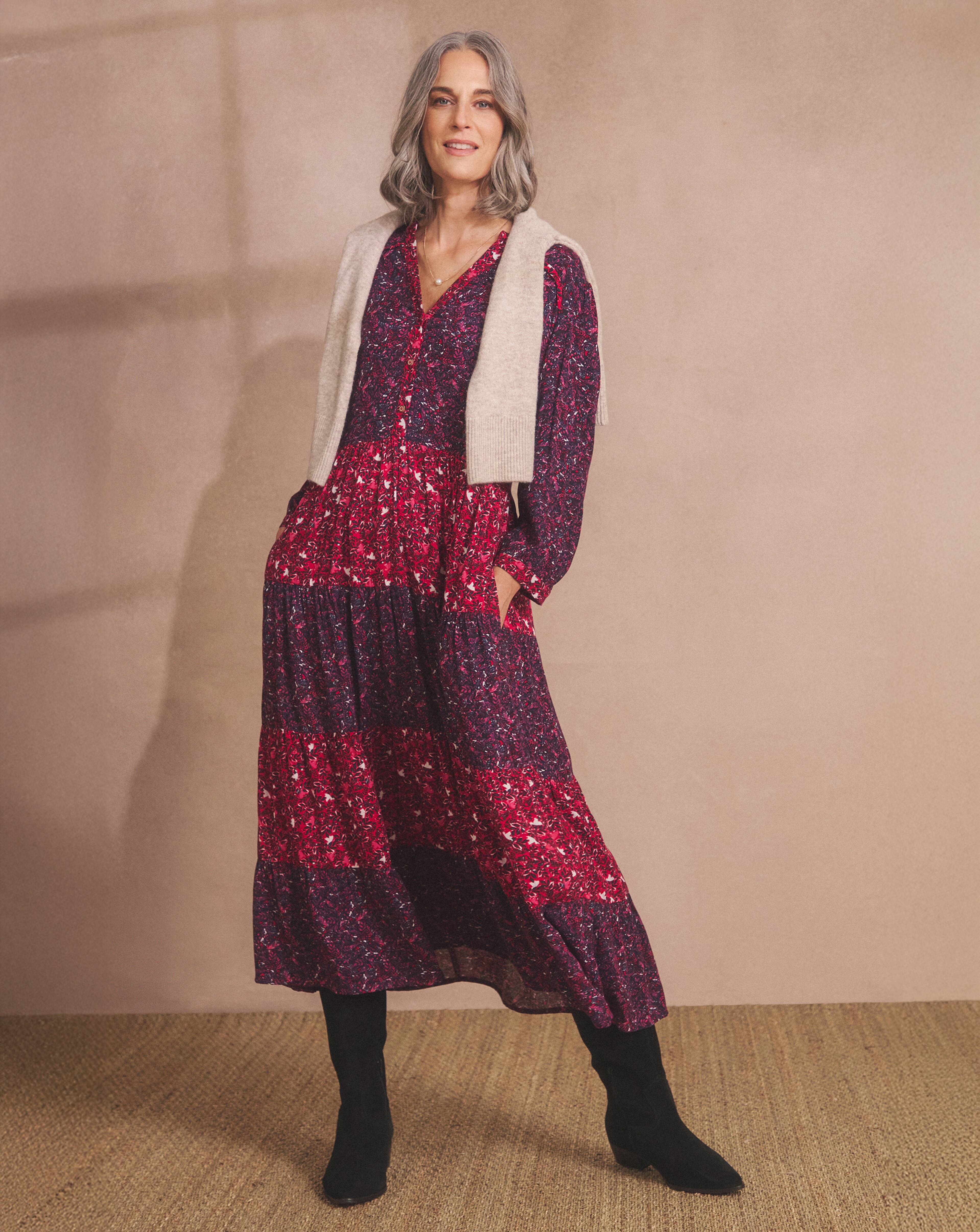 Person in a long red and purple patterned dress with a light vest and black boots. 