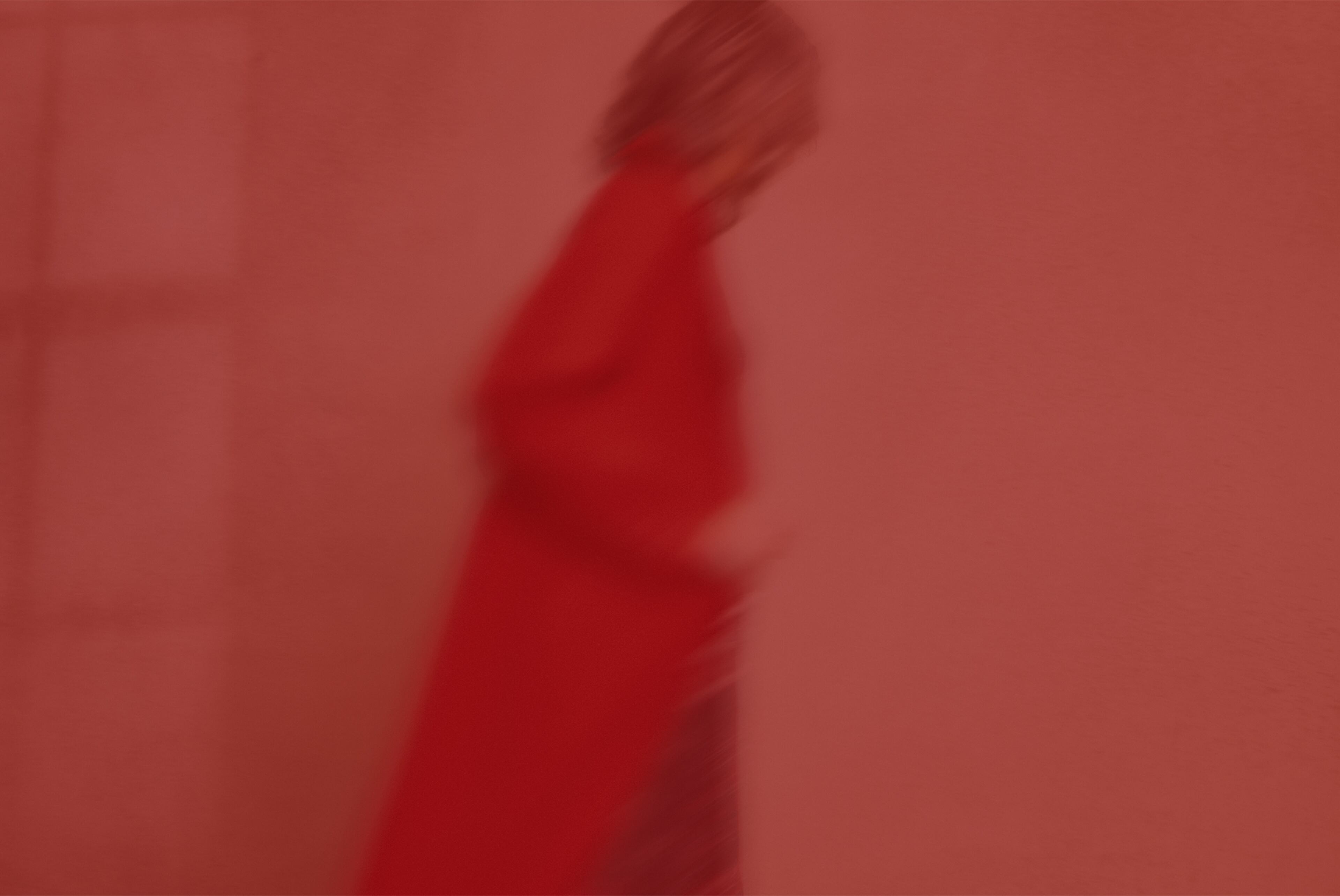 Blurred image of a model in a long red coat against a red-coloured background.