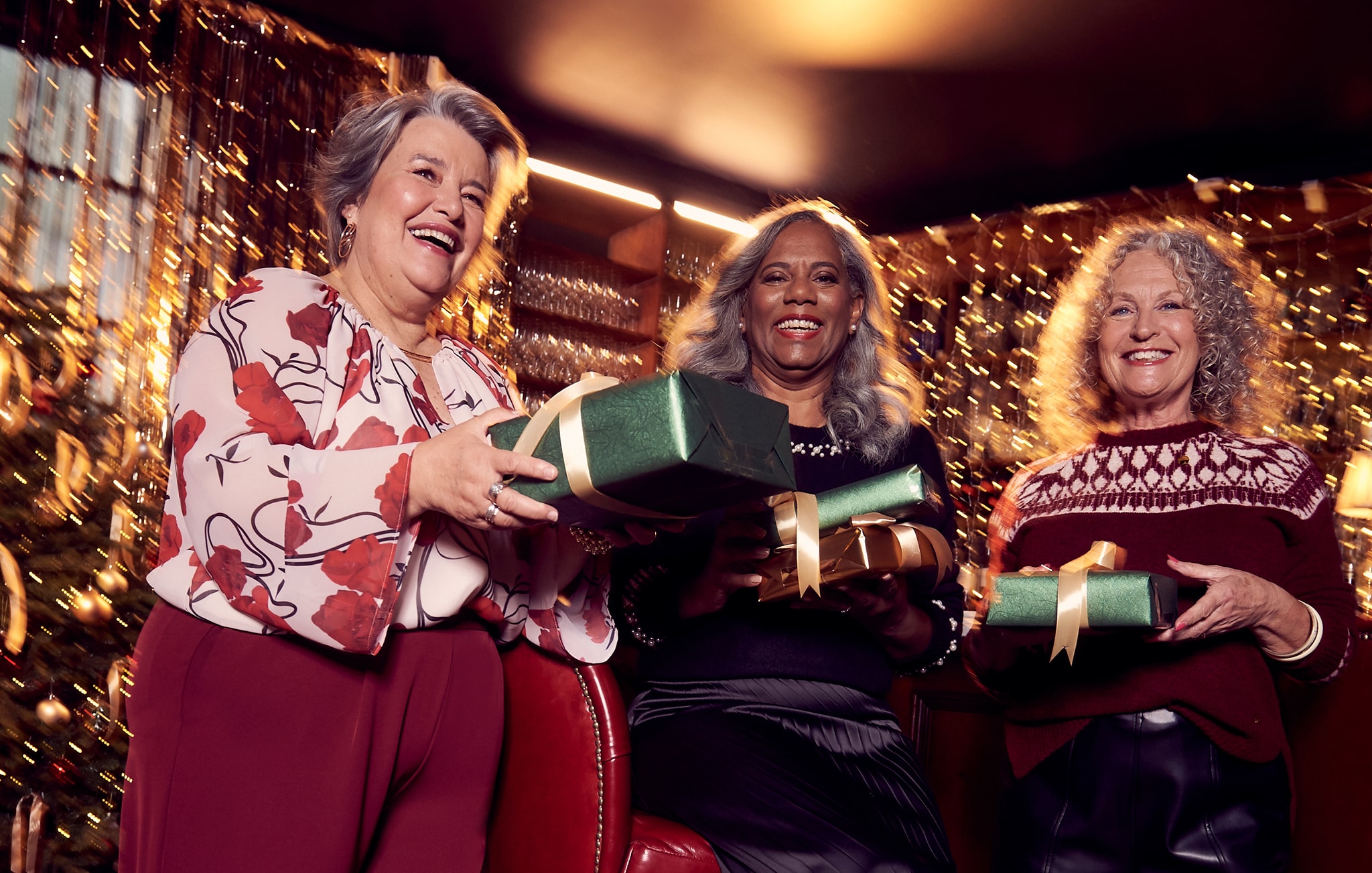 Three women wearing Christmas party outfits with Christmas presents