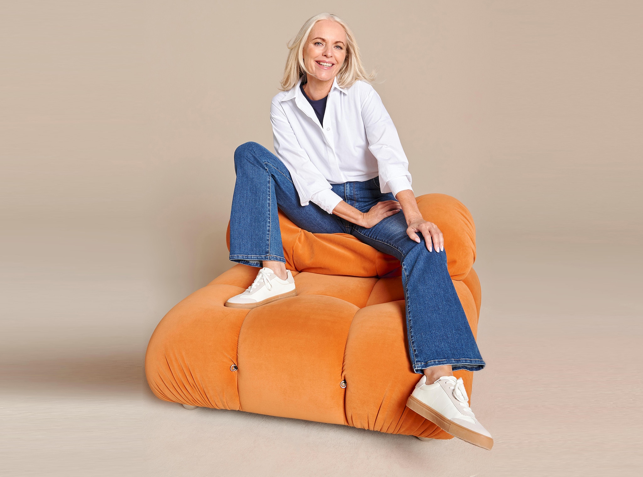 A woman wearing blue flared jeans and a white shirt sat on an orange sofa