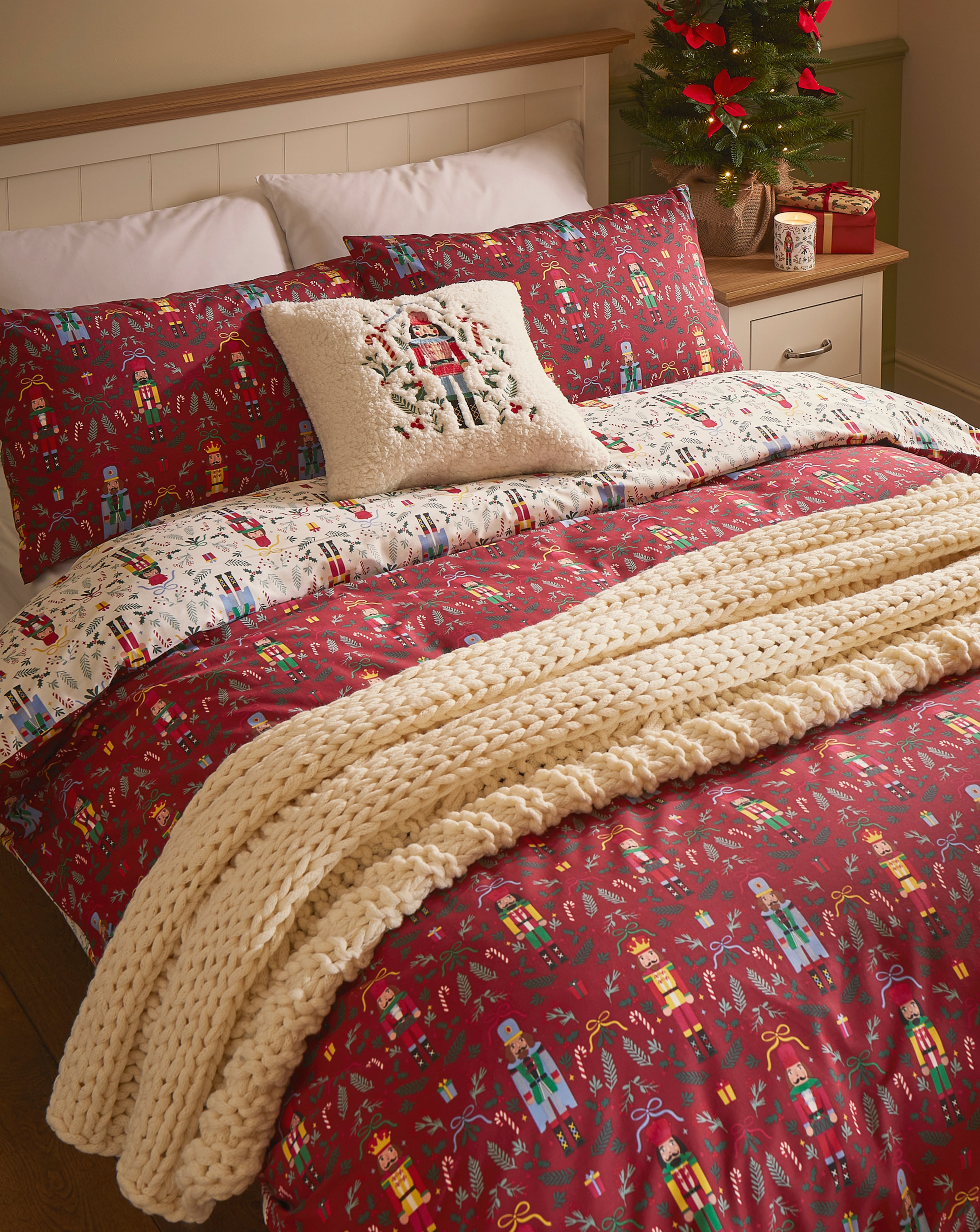 Festive bedroom with red and white nutcracker-themed bedding, a knitted blanket, and a small decorated Christmas tree on the bedside table