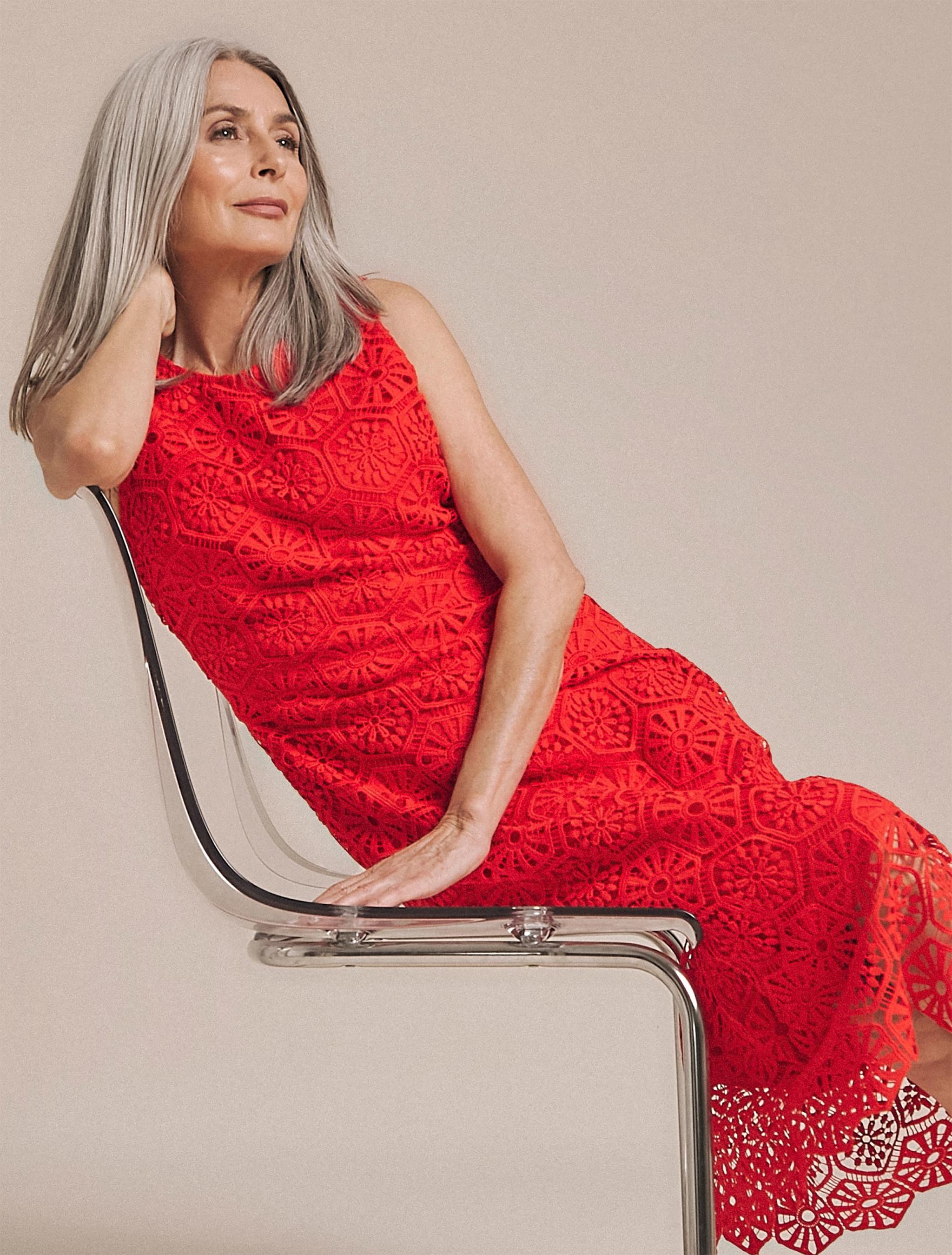 A woman sat on a chair wearing a long lacy red dress