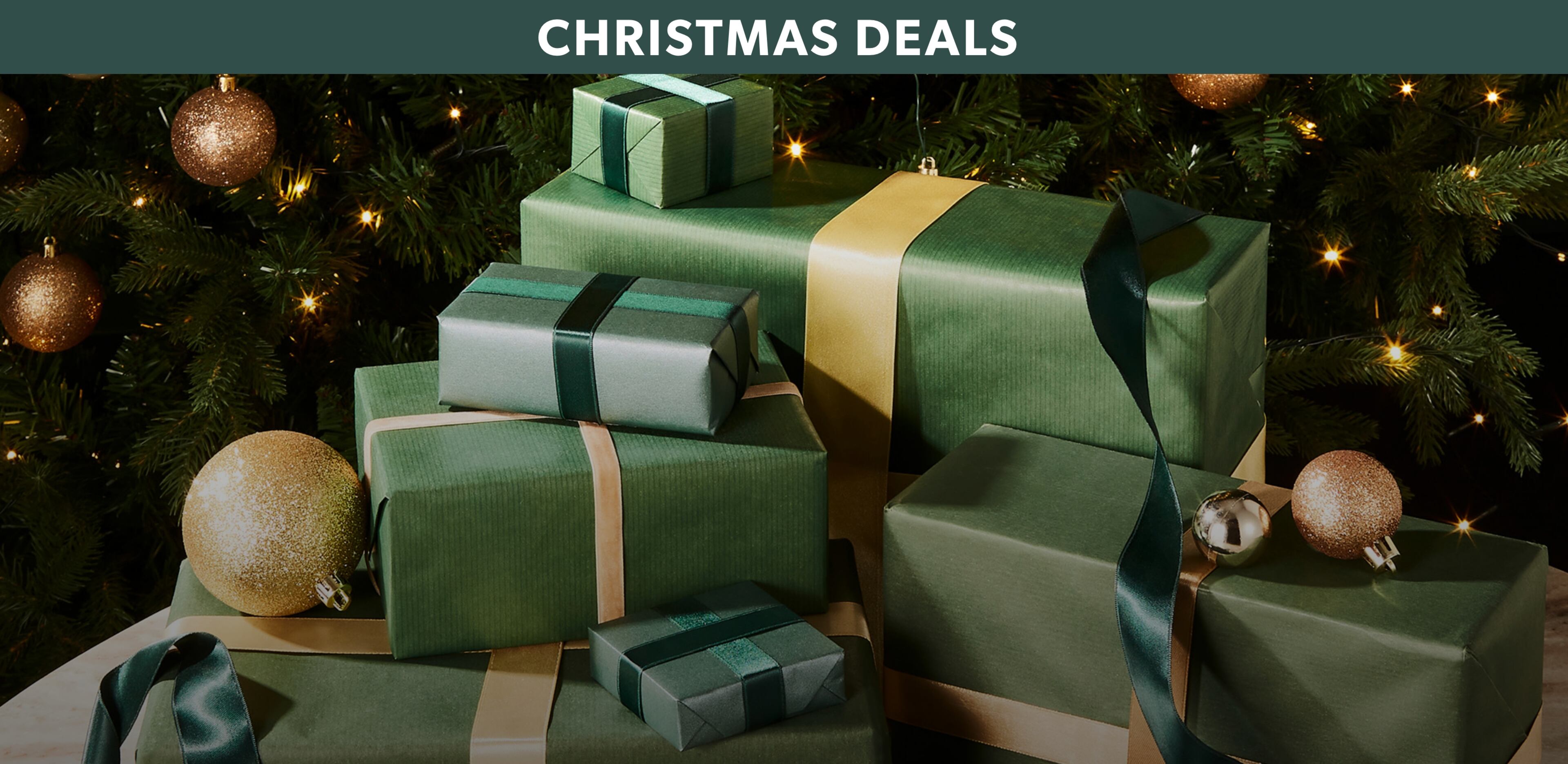 A stack of gift boxes wrapped in green paper, in front of a Christmas tree.