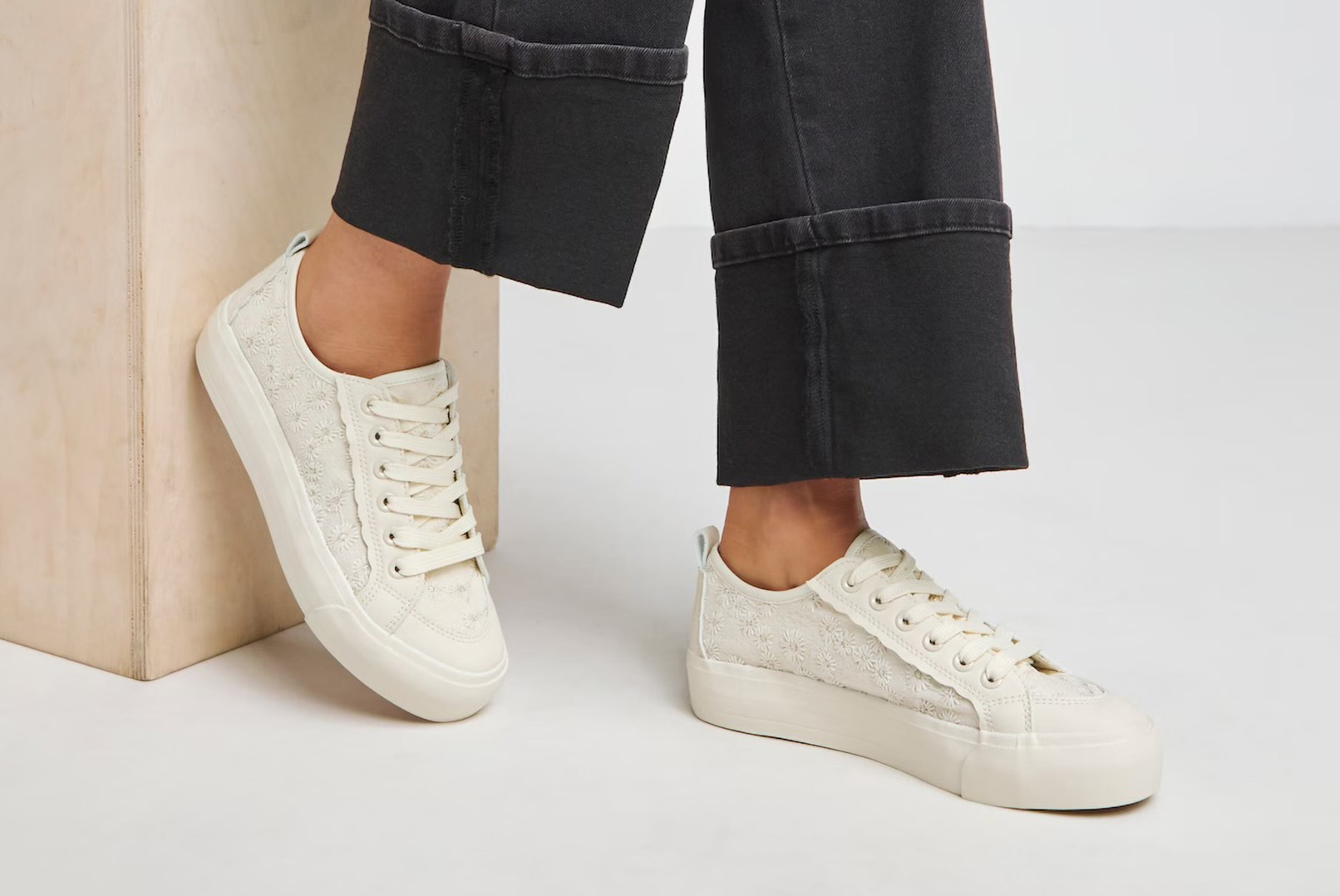 Model wearing cream coloured lace up trainers